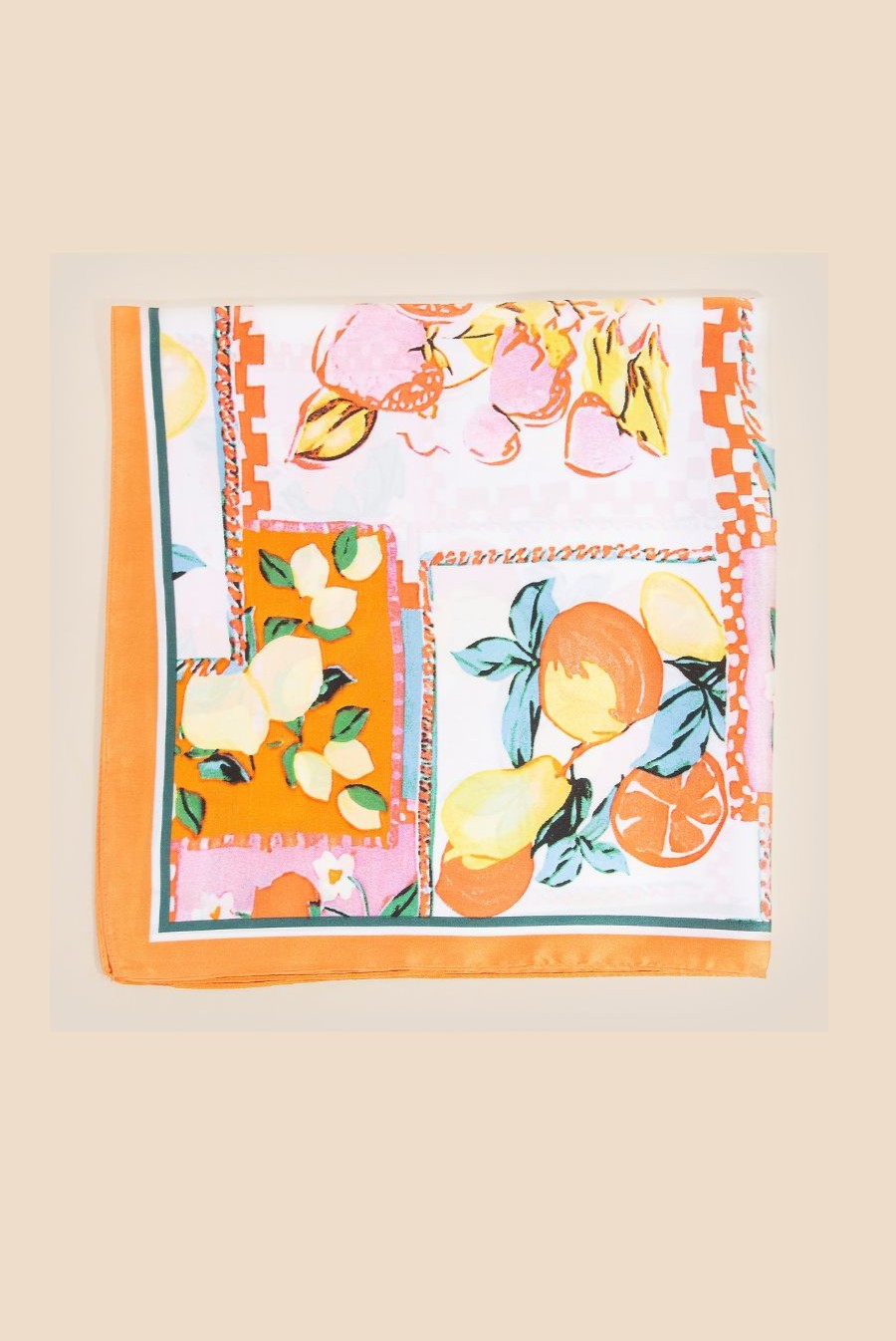 The South Moon Under Assorted Fruit Scarf in Orange Multi is a square bandana with lemons, pears, and oranges in a patchwork design and orange border, shown folded on a beige background.