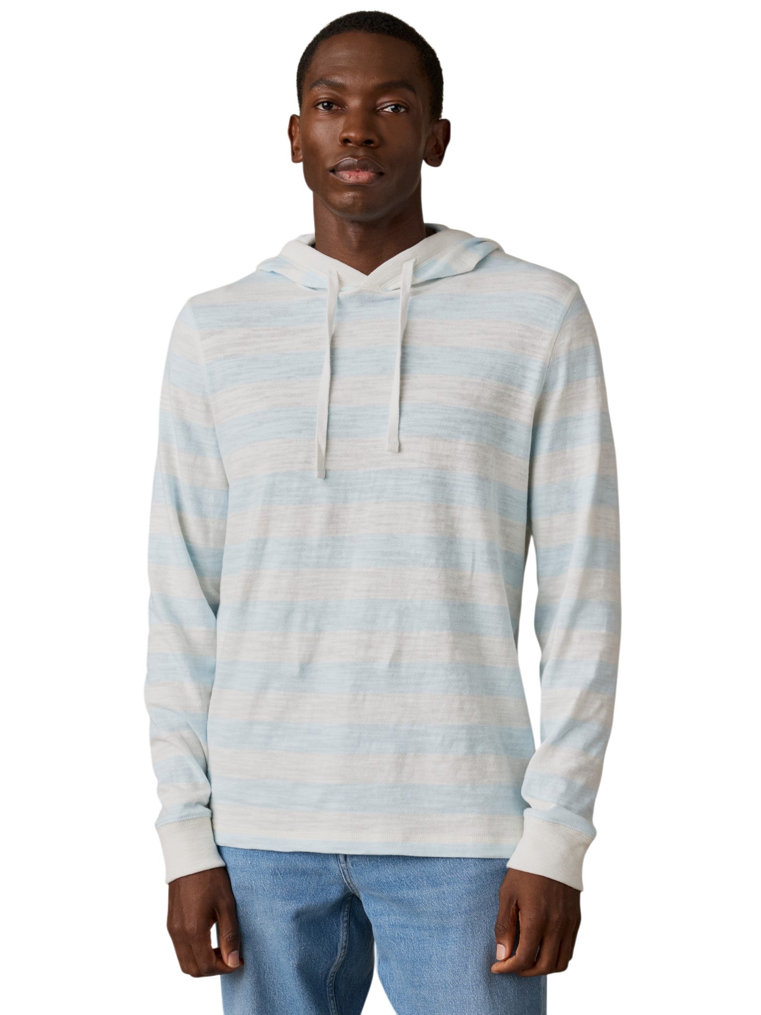 A man stands facing forward against a plain white background, wearing the Faherty Sunwashed Slub Hoodie in Blue Multi with a drawstring hood and long sleeves, paired with light blue jeans.