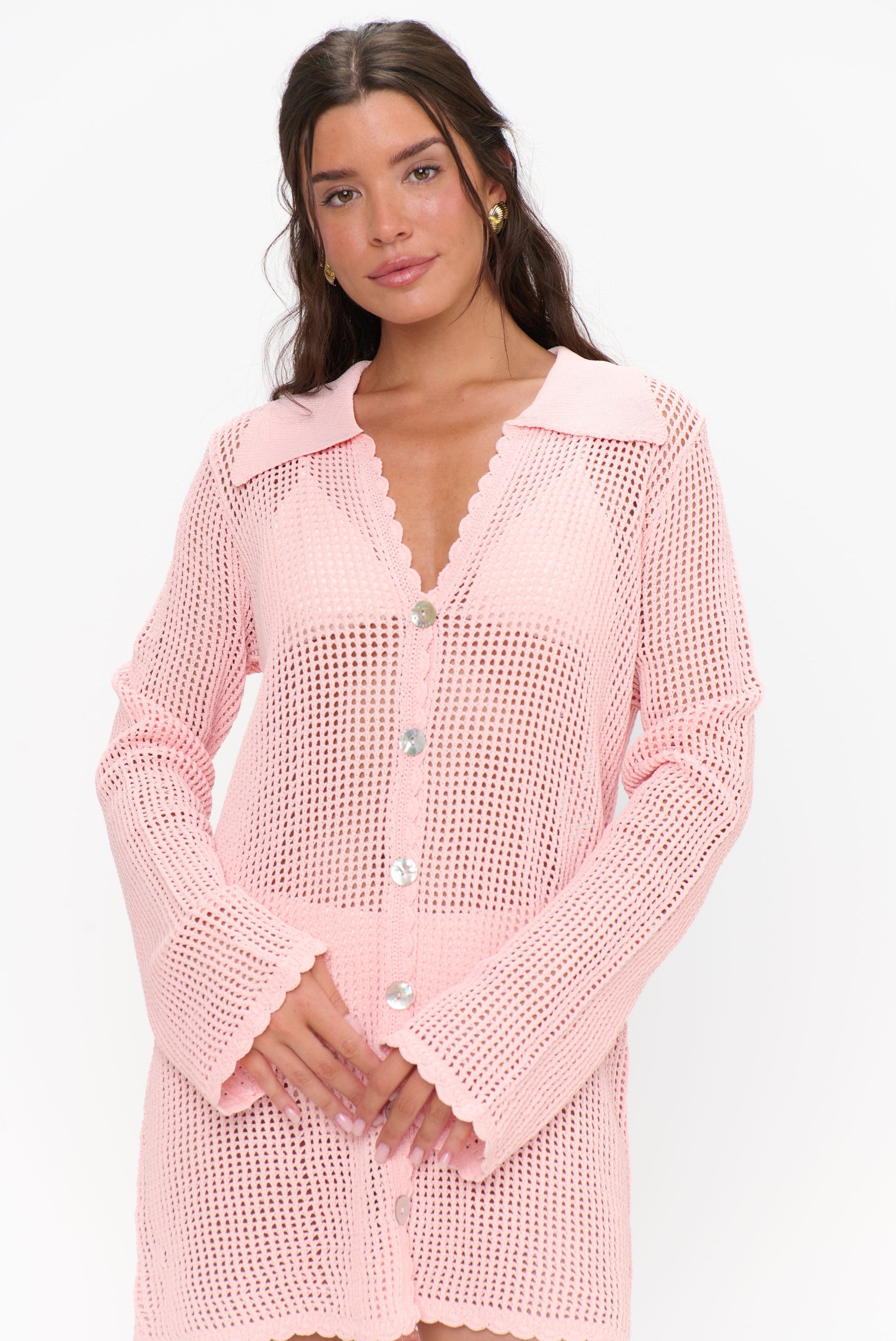 A woman wears the Show Me Your Mumu Button Up Coverup, a peachy pink crochet dress with scalloped collar and cuffs, standing against a white background.