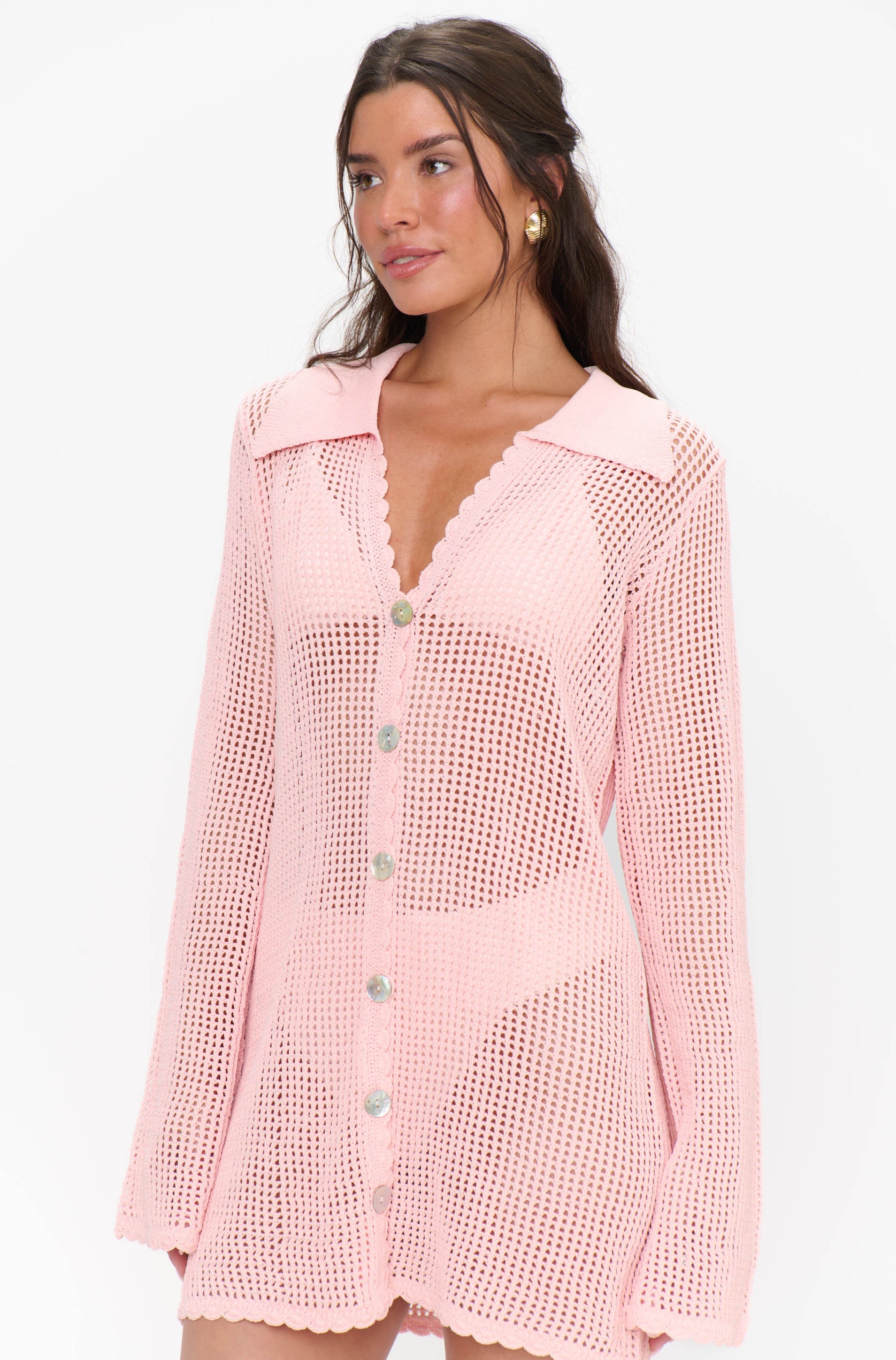 A woman models the Show Me Your Mumu Button Up Coverup in peachy pink, featuring a crochet design, scalloped hem, and collar. Her long brown hair is styled in loose waves as she stands against a white background.