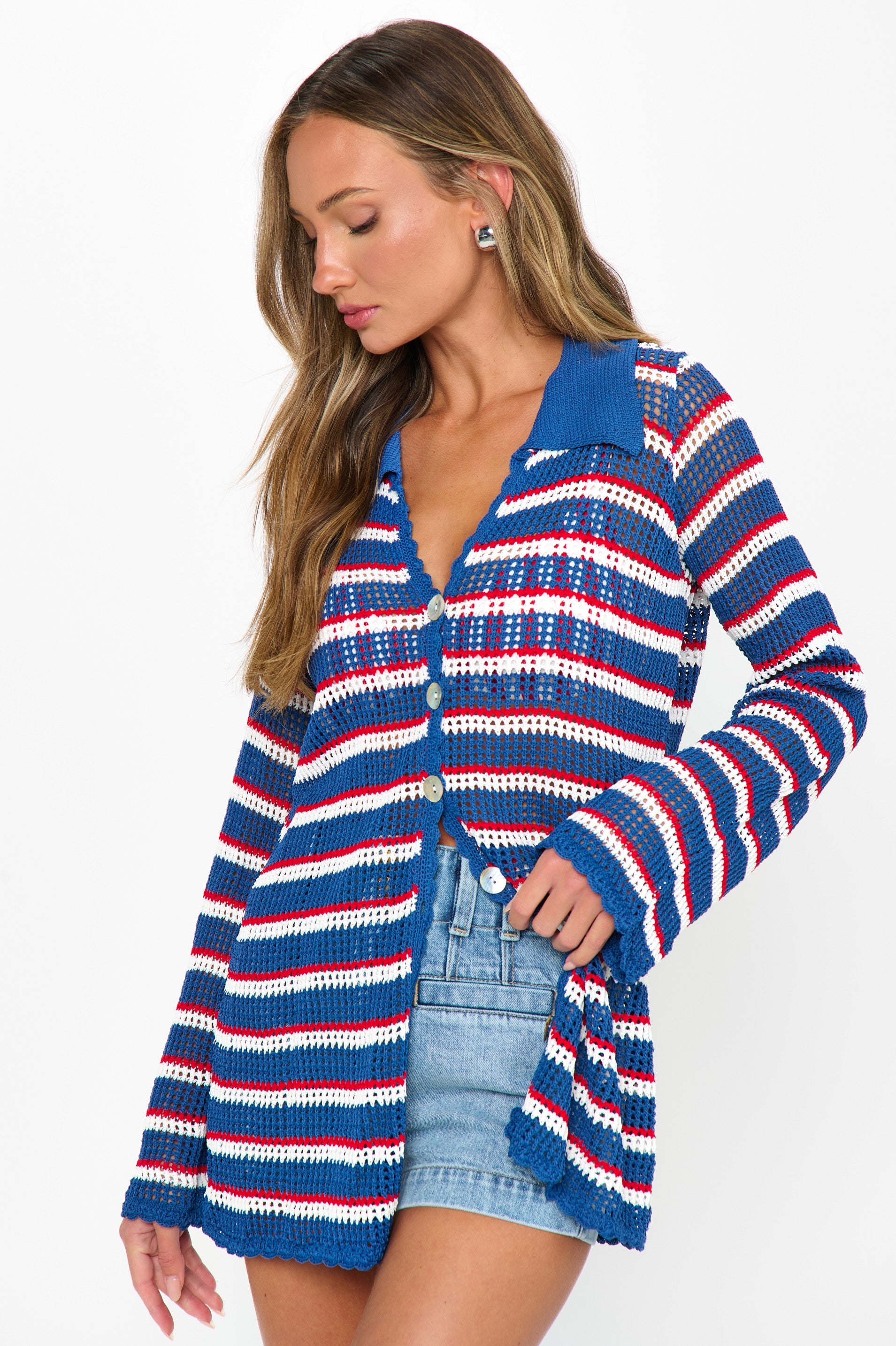 A woman models the Show Me Your Mumu Button Up Coverup—a blue, white, and red striped cardigan—over a blue top and denim shorts against a white background, creating a perfect look for your summer wardrobe.