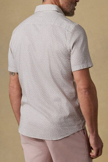 A man is shown from the back wearing a Faherty Short Sleeve Movement Monterrey Shirt and light pink shorts against a plain beige background.