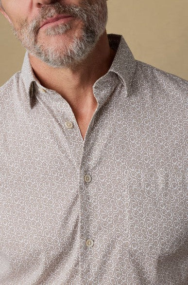 A man with a gray beard wears the Faherty Short Sleeve Movement Monterrey Shirt, featuring a light-colored pattern and spread collar. The image, shot against a neutral background, is cropped from his nose down to his upper torso.