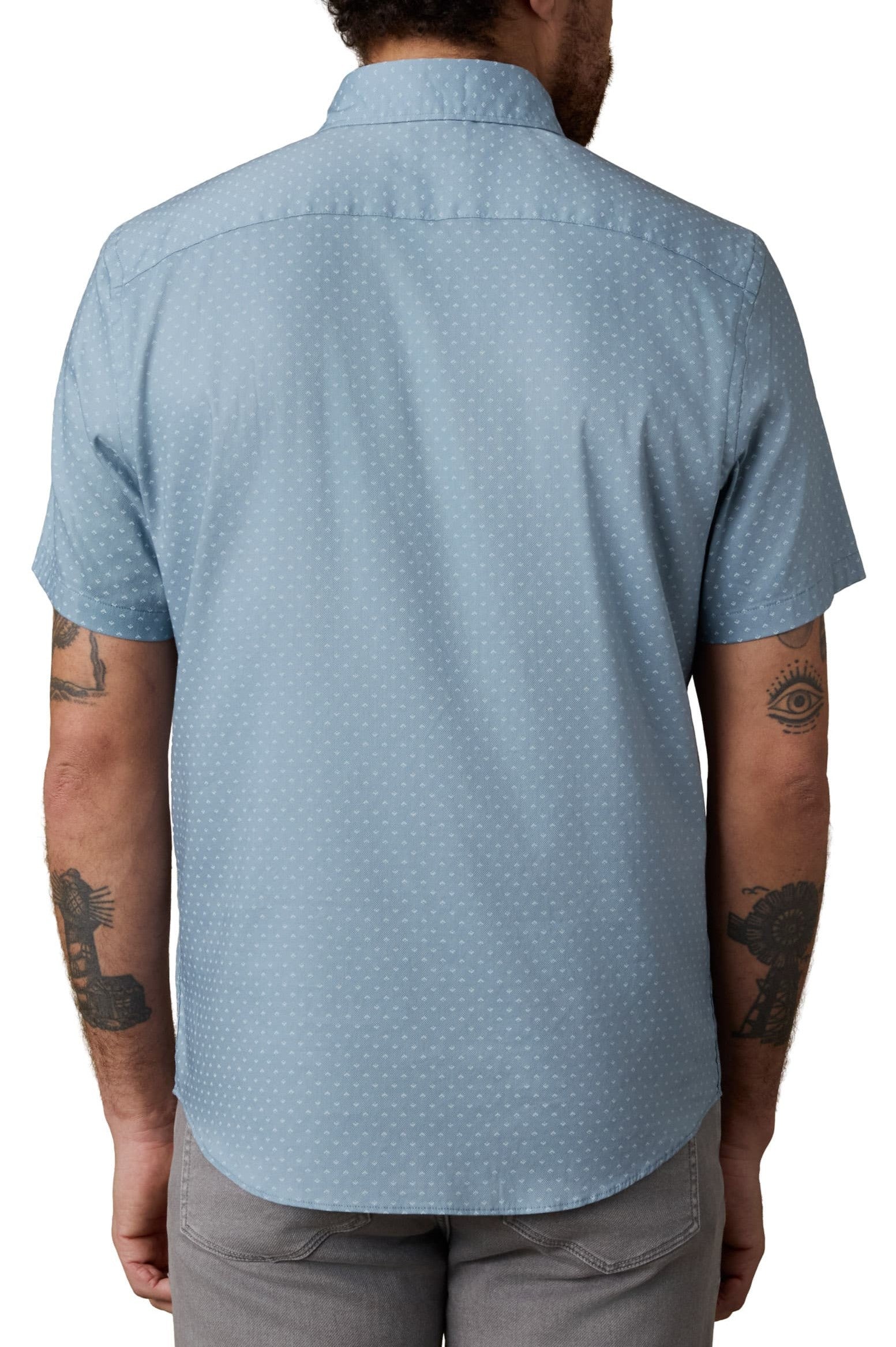 A tattooed person is seen from behind wearing a relaxed fit Faherty Short Sleeve Movement Monterrey Shirt with a subtle dotted pattern, spread collar, and light gray pants.