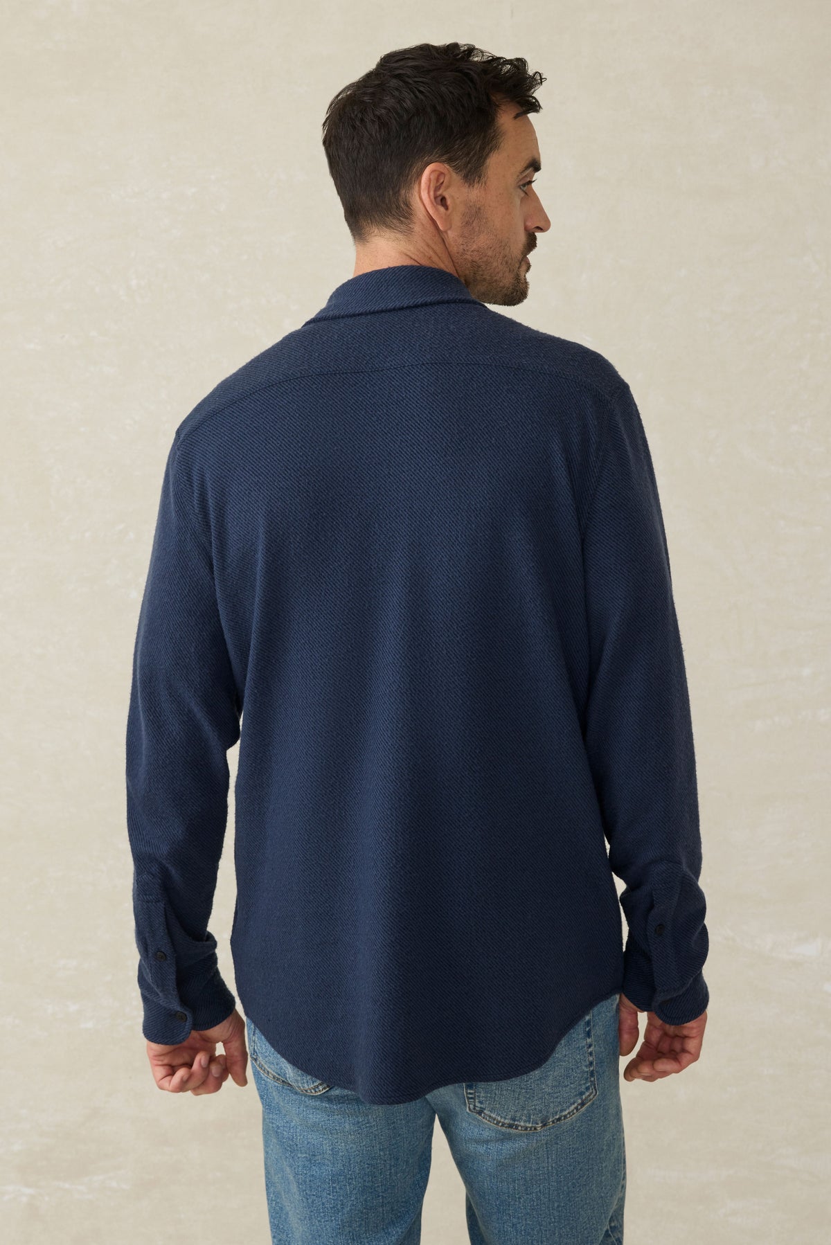 Man wearing dark navy textured sweater shirt with collar, shown from back view, paired with blue jeans.