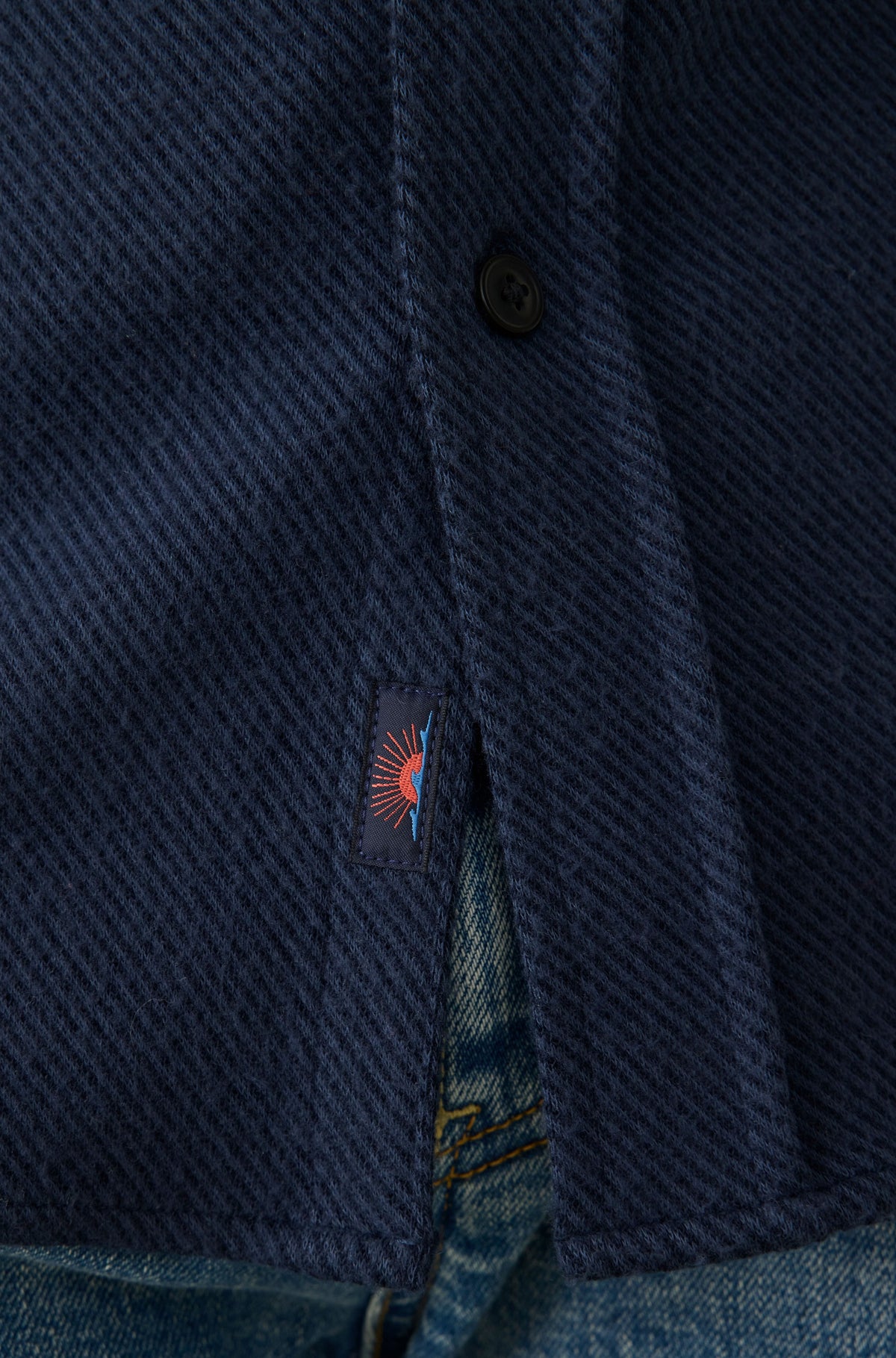 Dark blue textured sweater shirt with button closure and embroidered sun design on chest pocket.
