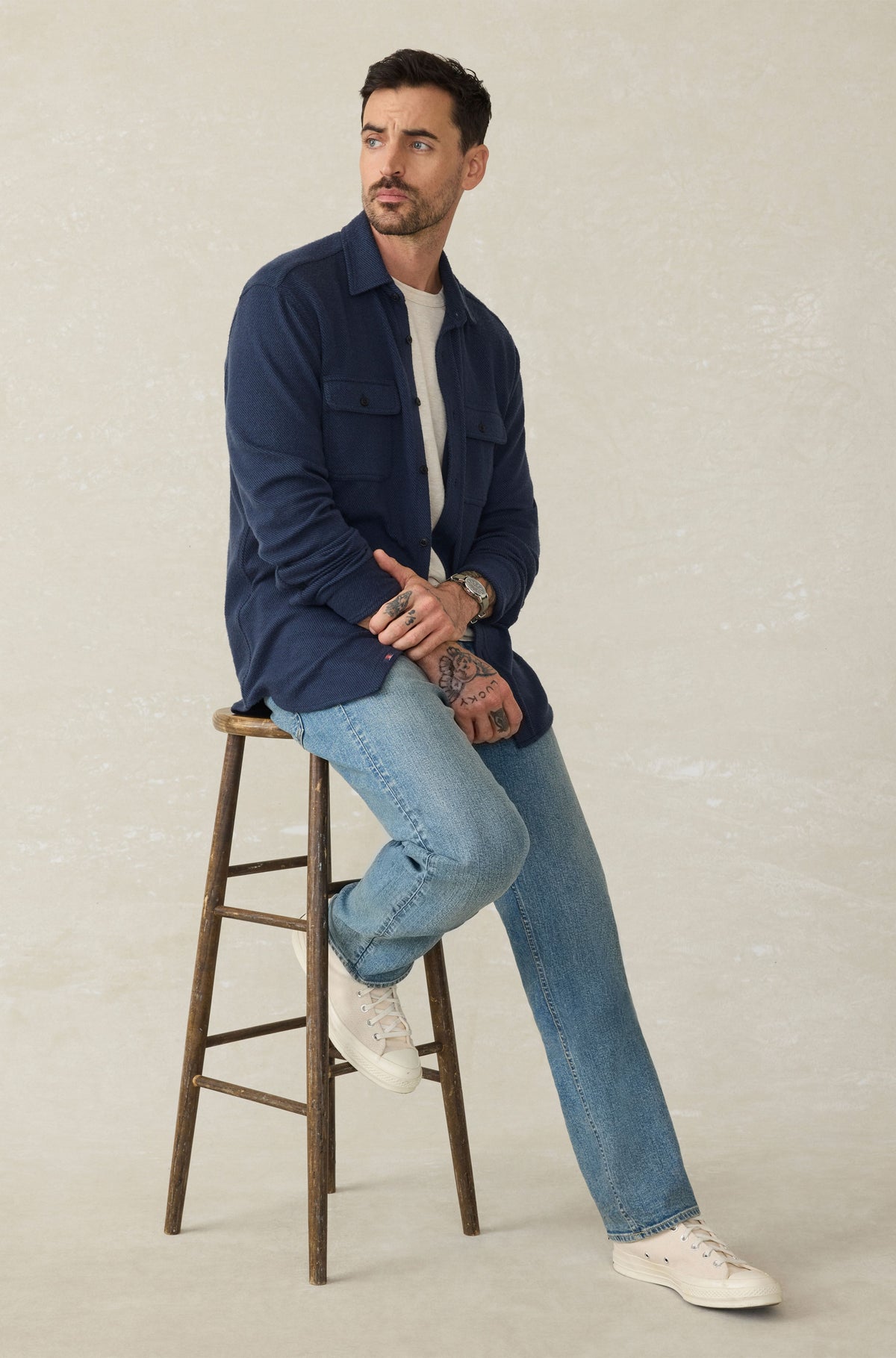 Man wearing navy button-up sweater shirt over white undershirt, paired with light blue jeans and white sneakers.
