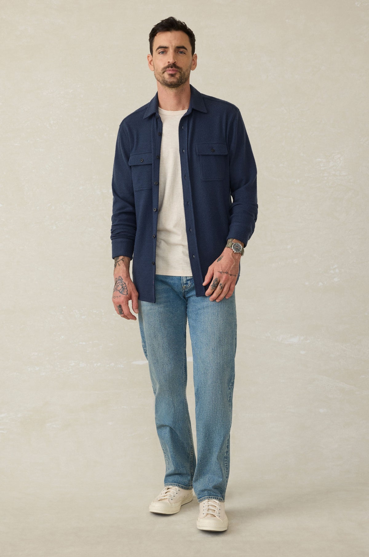 Man wearing dark navy button-up sweater shirt over white t-shirt, paired with light blue jeans and white sneakers.