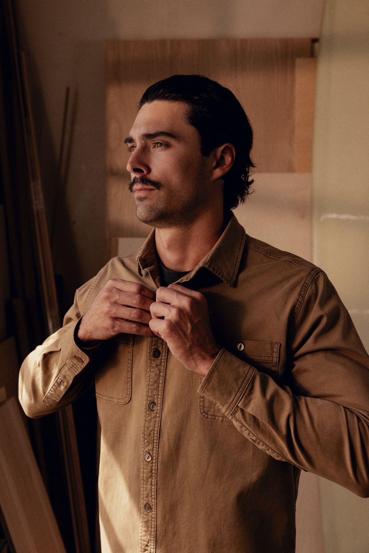 Tan long-sleeve button-up shirt with chest pockets worn over a black undershirt.