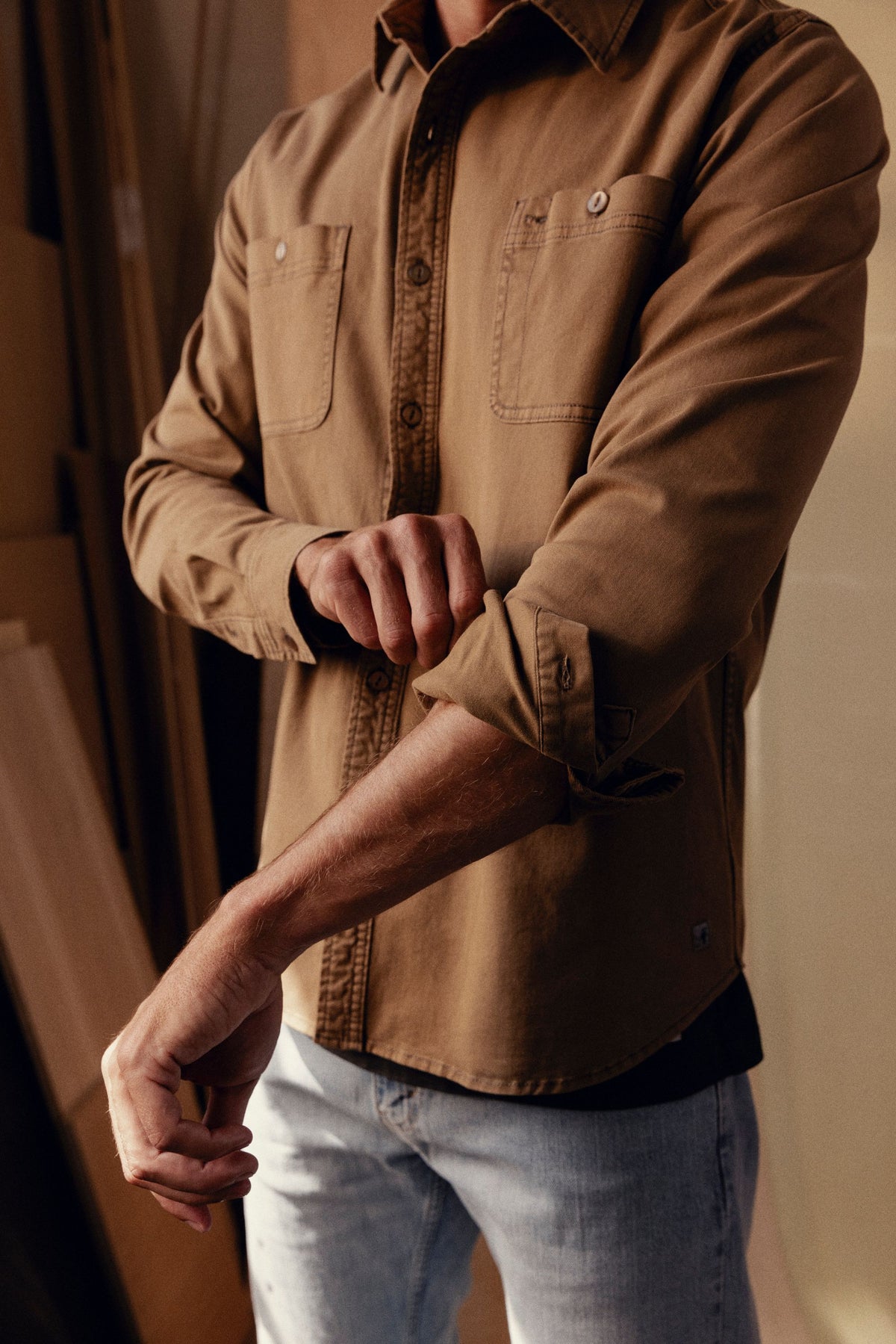 Tan long-sleeve button-up shirt with chest pockets, worn over light gray pants.