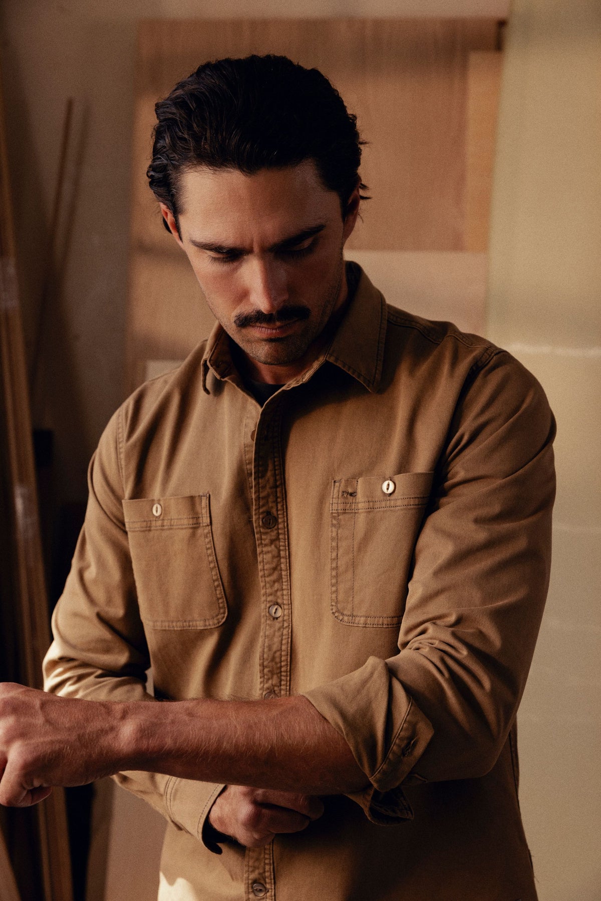 Tan long-sleeve button-up shirt with chest pockets and contrasting stitching, worn by man looking downward.