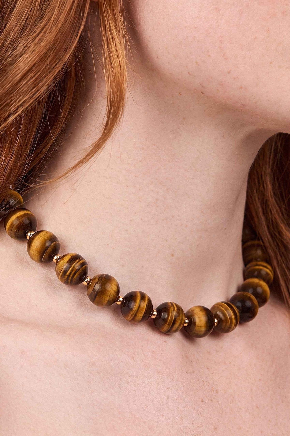 Tiger's eye stone beads with striped golden-brown patterns separated by silver spacers worn as a necklace.