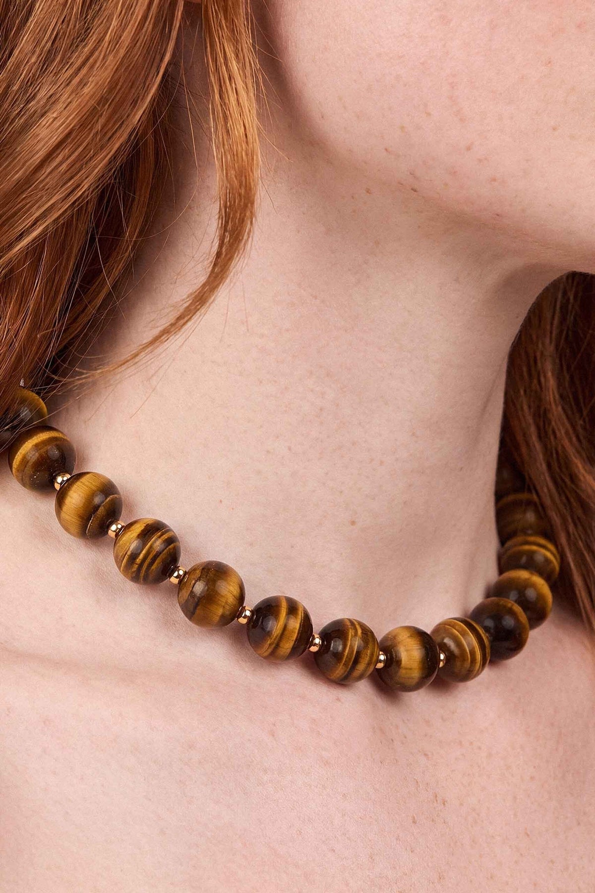 Brown tiger eye stone beads with silver spacers on a beaded necklace worn close to the neck.