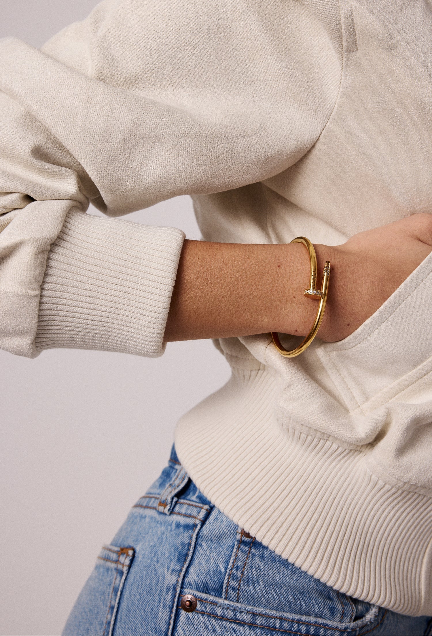 A person wearing a light jacket and blue jeans reveals a 4mm thick, 14kt gold plated Nailed It Bracelet by Electric Picks on their wrist.