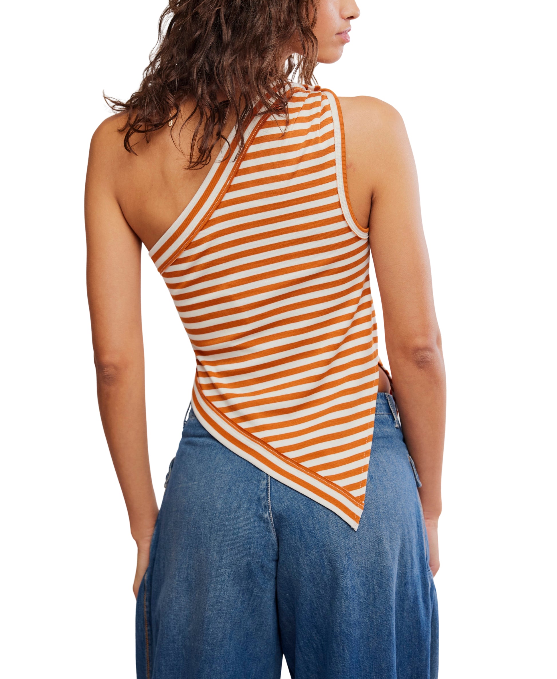 A woman is seen from the back against a white background, wearing the Free People Knot My Vibe in Butter Pecan—an orange and white striped, one-shoulder top with an asymmetrical hem—paired with blue jeans.