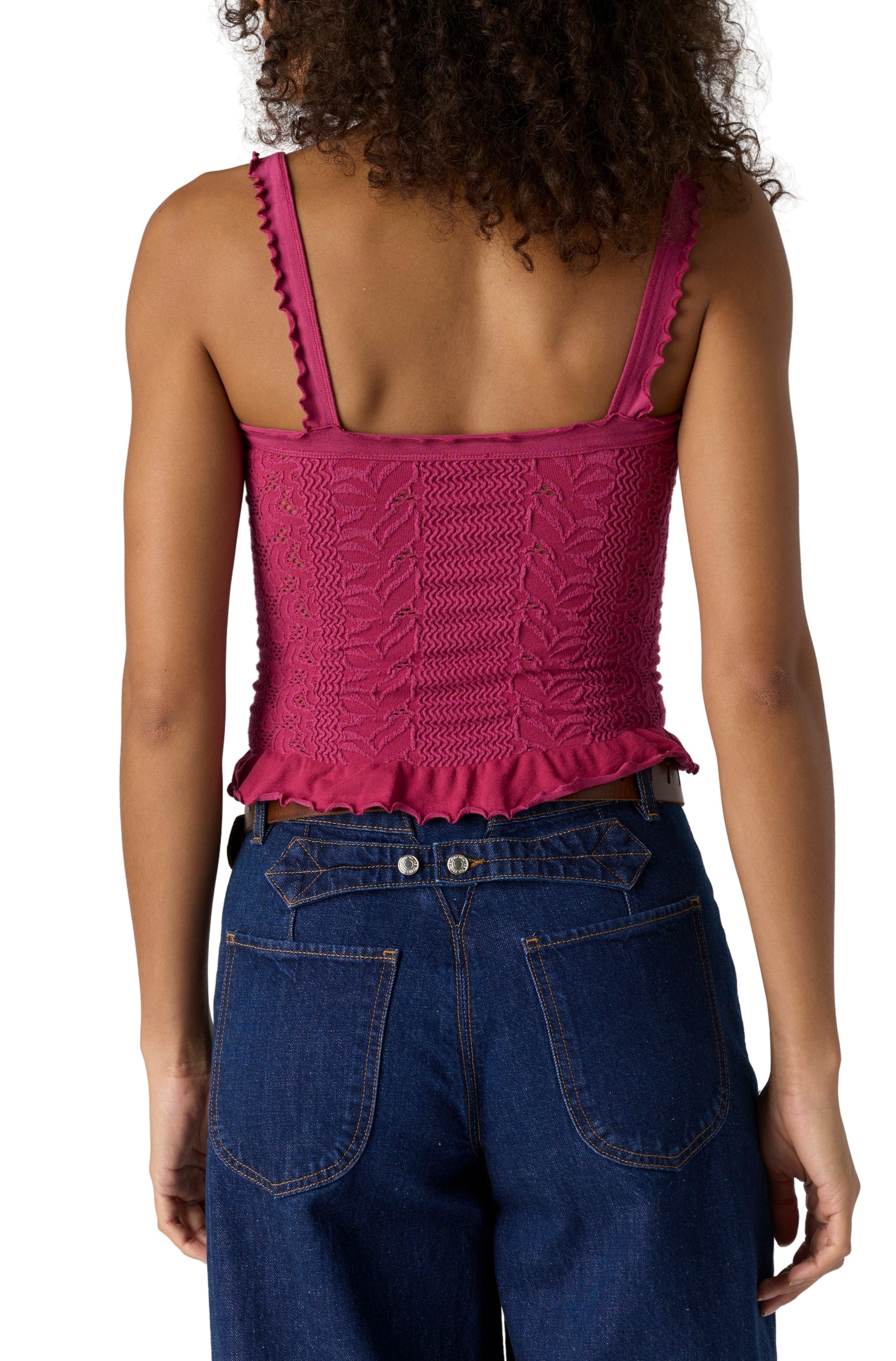 A person with curly hair is seen from the back, wearing Free People's So Soft Femme Square Neck magenta textured sleeveless top and high-waisted blue jeans with large back pockets and belt loops.