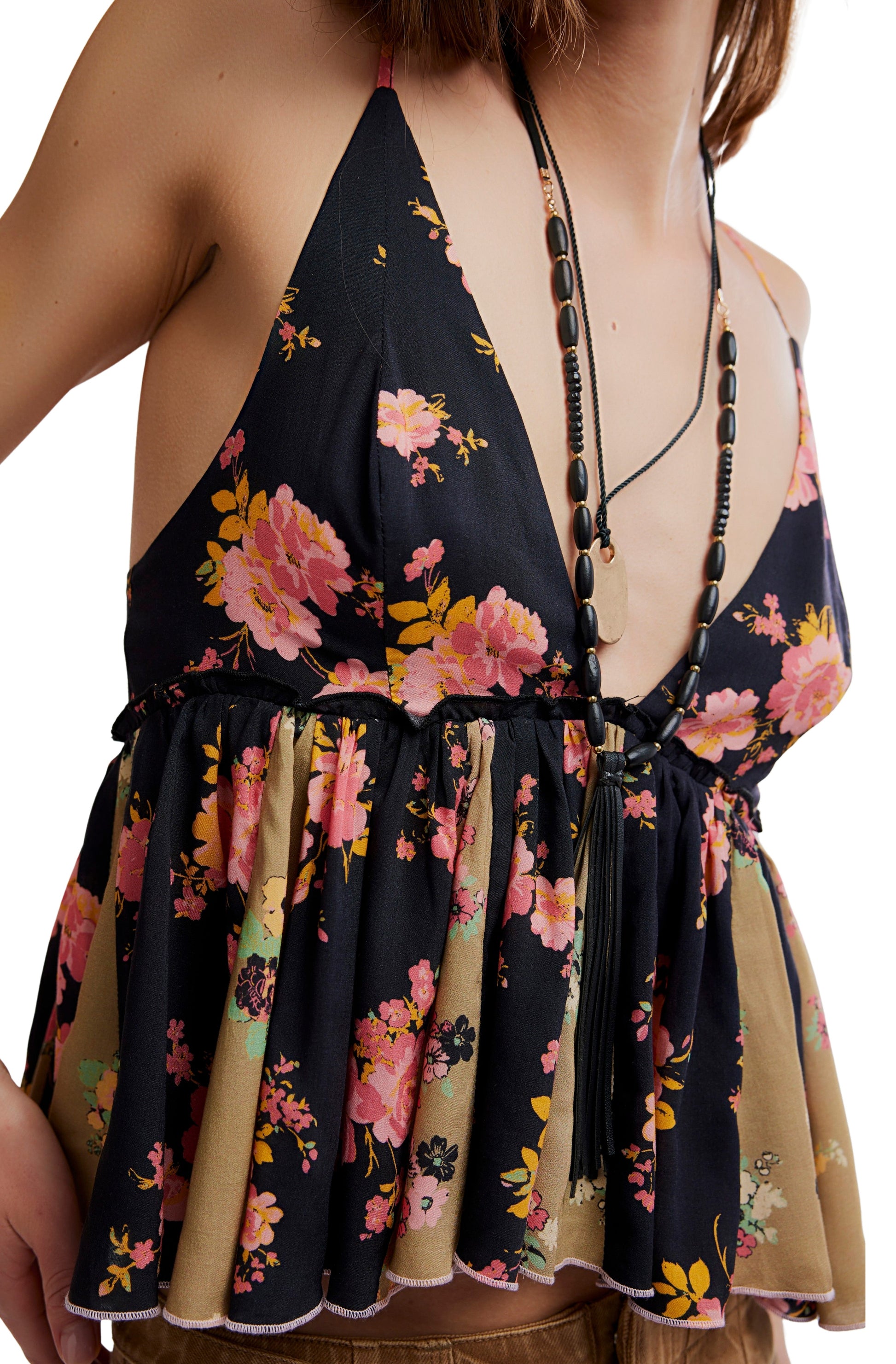 A person wears the Free People Tillie Top—a sleeveless, low-cut floral top with adjustable straps, ruffled hem, and pink/yellow flowers on a dark background—paired with a long beaded necklace. Head is out of frame.