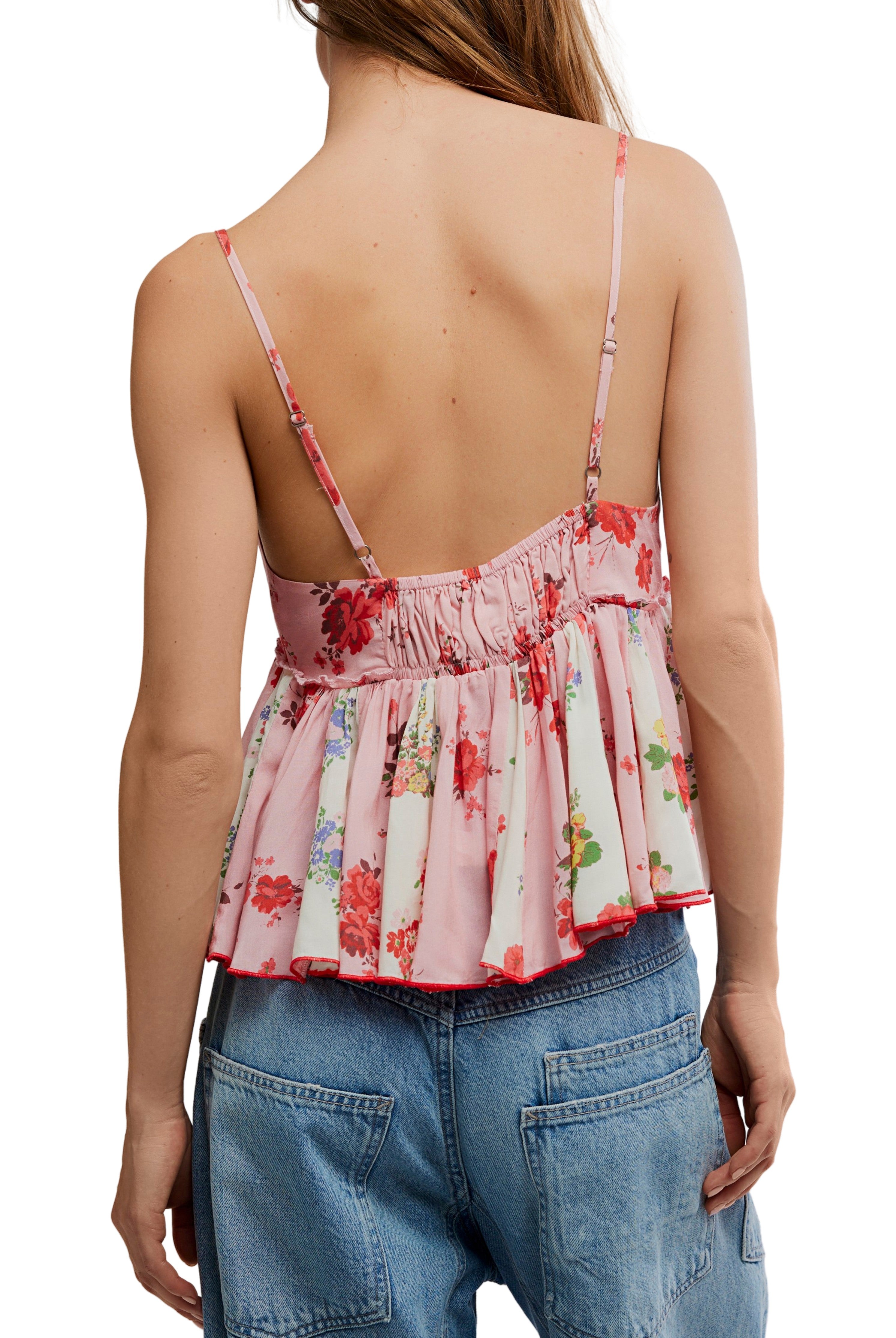 A woman is shown from behind wearing the Free People Tillie Top, a pink floral spaghetti strap top with adjustable straps and a low, ruched back, paired with blue high-waisted jeans. Her hair is down.