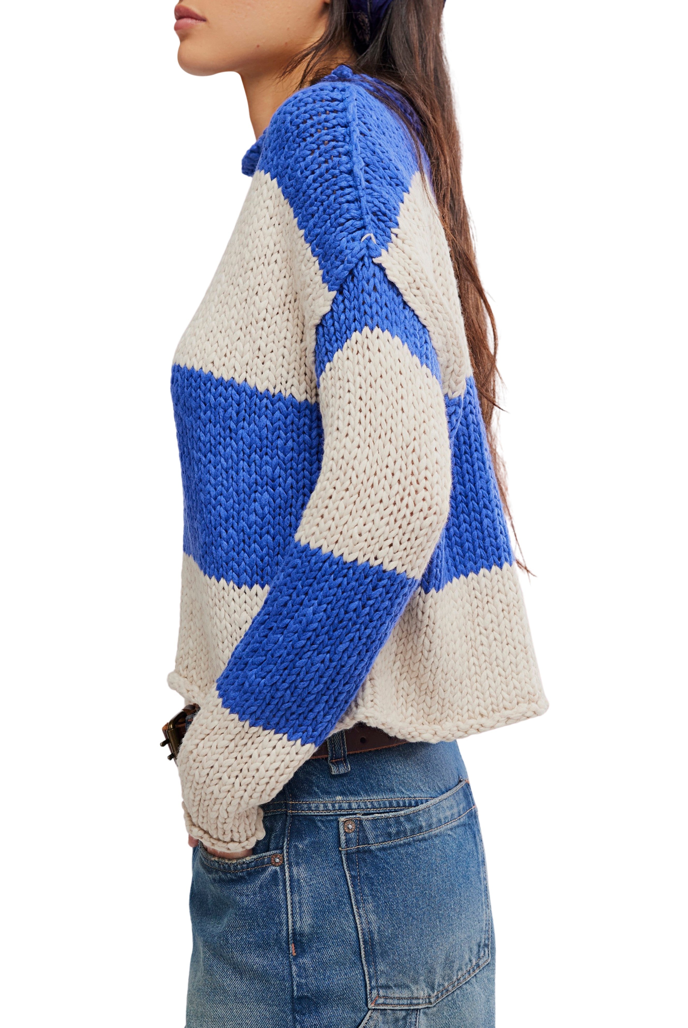 A woman in profile wears the Opal Rugby Stripe Sweater by Free People—a boxy fit, chunky knit with wide blue and beige stripes—paired with blue denim jeans. Her long hair is loose, and she stands against a white background.
