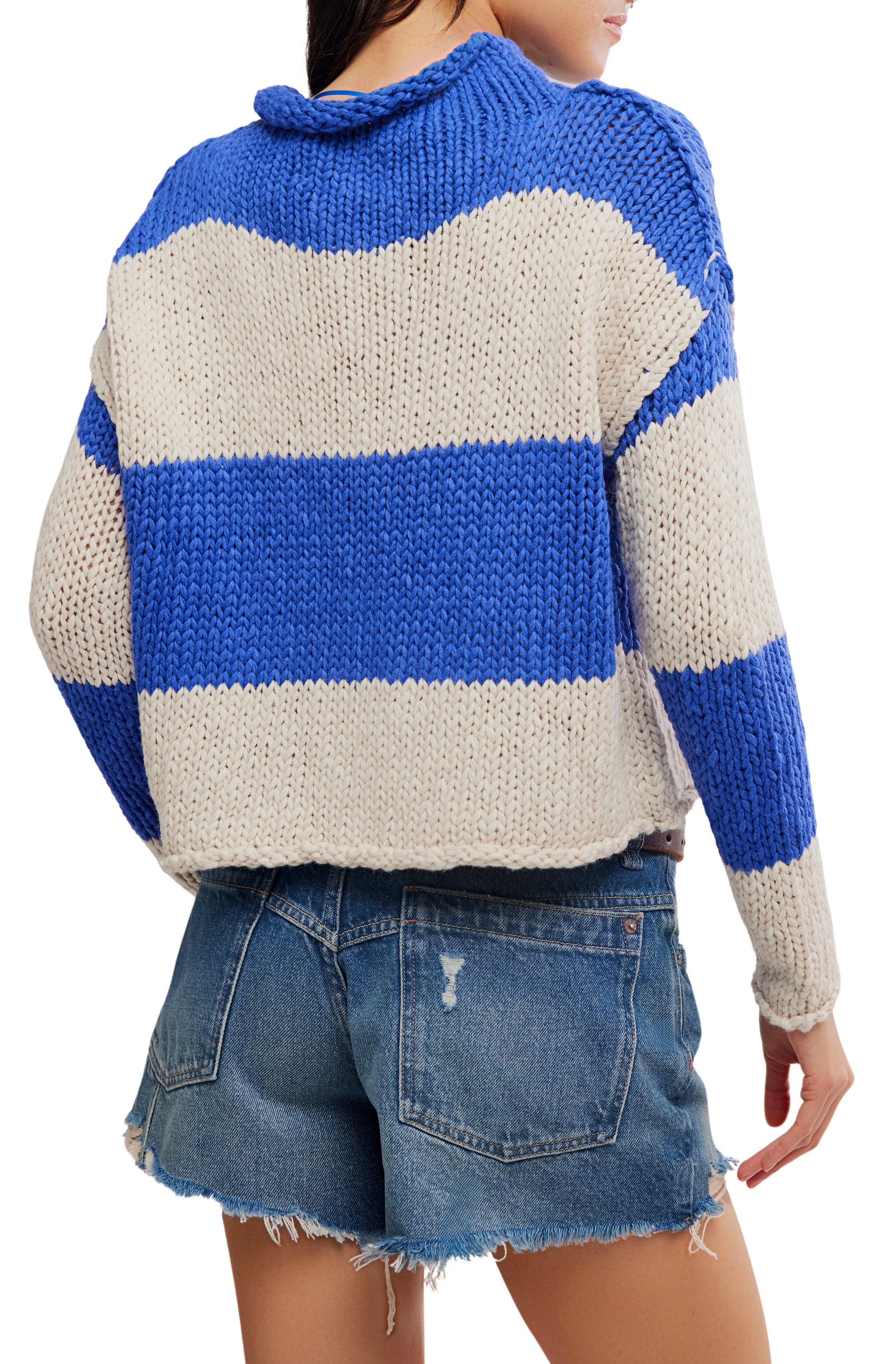 A person shown from the back wearing the Free People Opal Rugby Stripe Sweater—a blue and white striped cotton knit with a boxy fit—paired with distressed denim shorts.