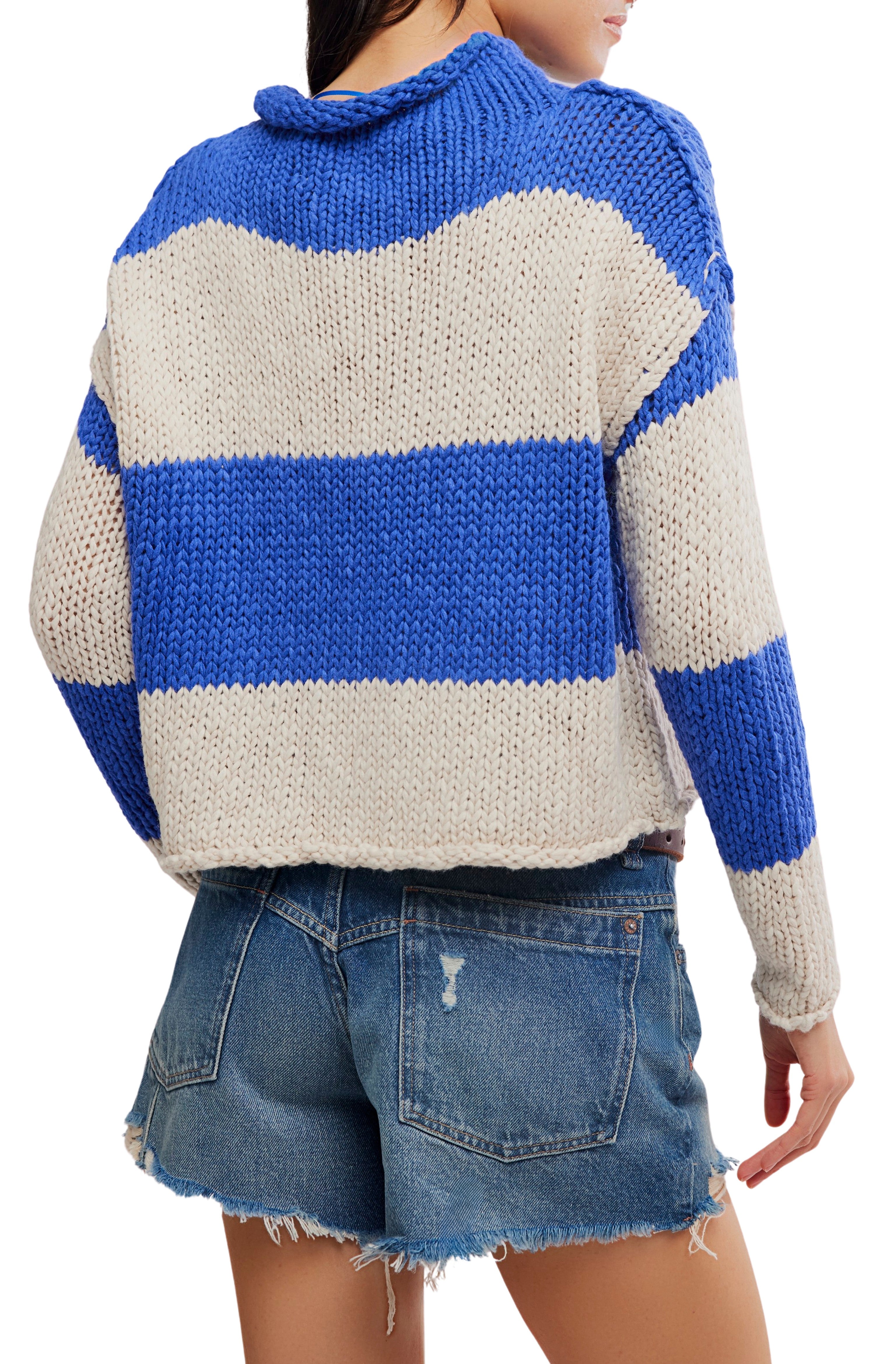 A person shown from the back wearing the Free People Opal Rugby Stripe Sweater—a blue and white striped cotton knit with a boxy fit—paired with distressed denim shorts.