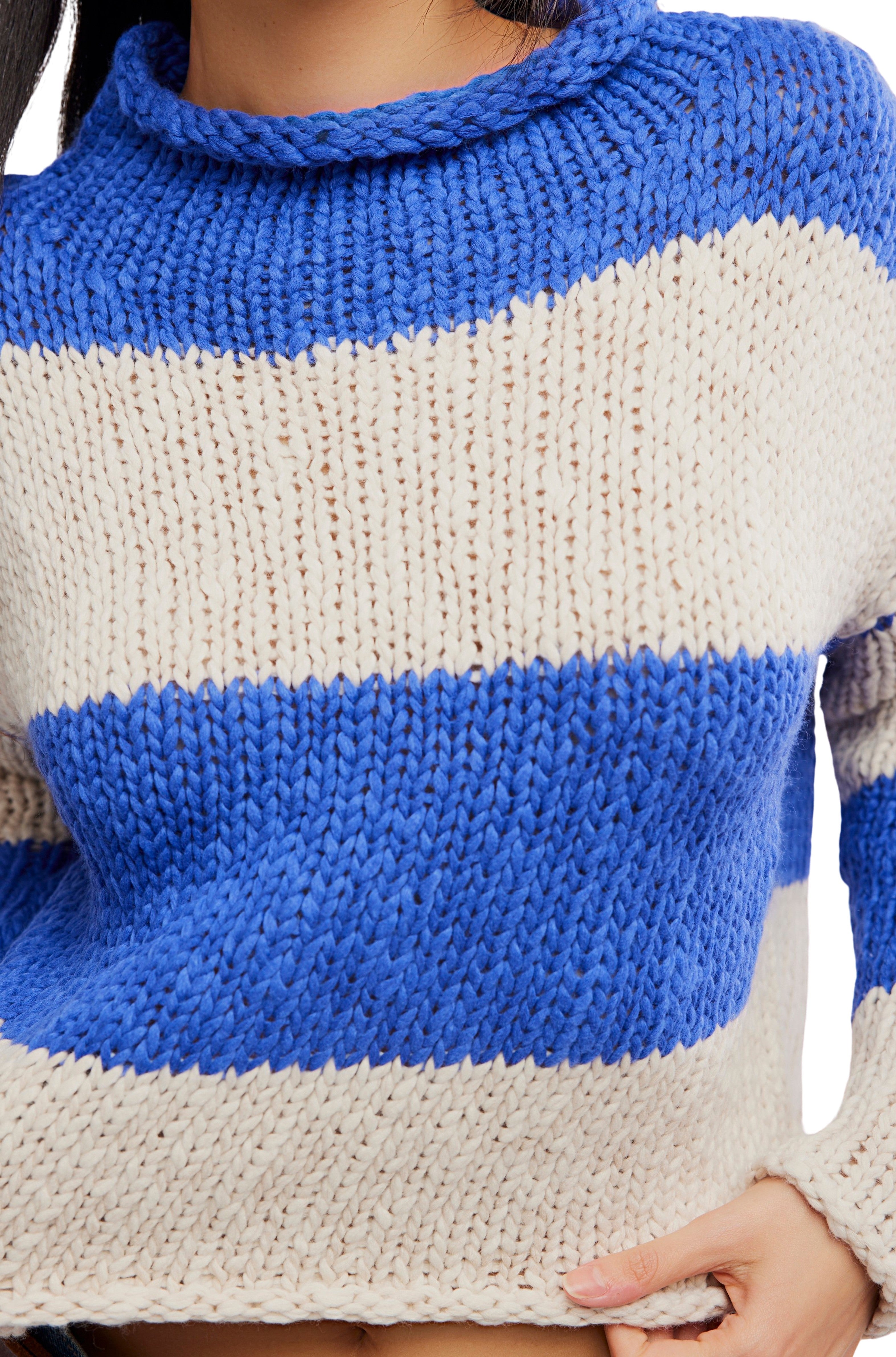 A person wearing the Free People Opal Rugby Stripe Sweater, a boxy fit chunky knit with wide horizontal blue and cream stripes. Only their lower face and upper body are visible.