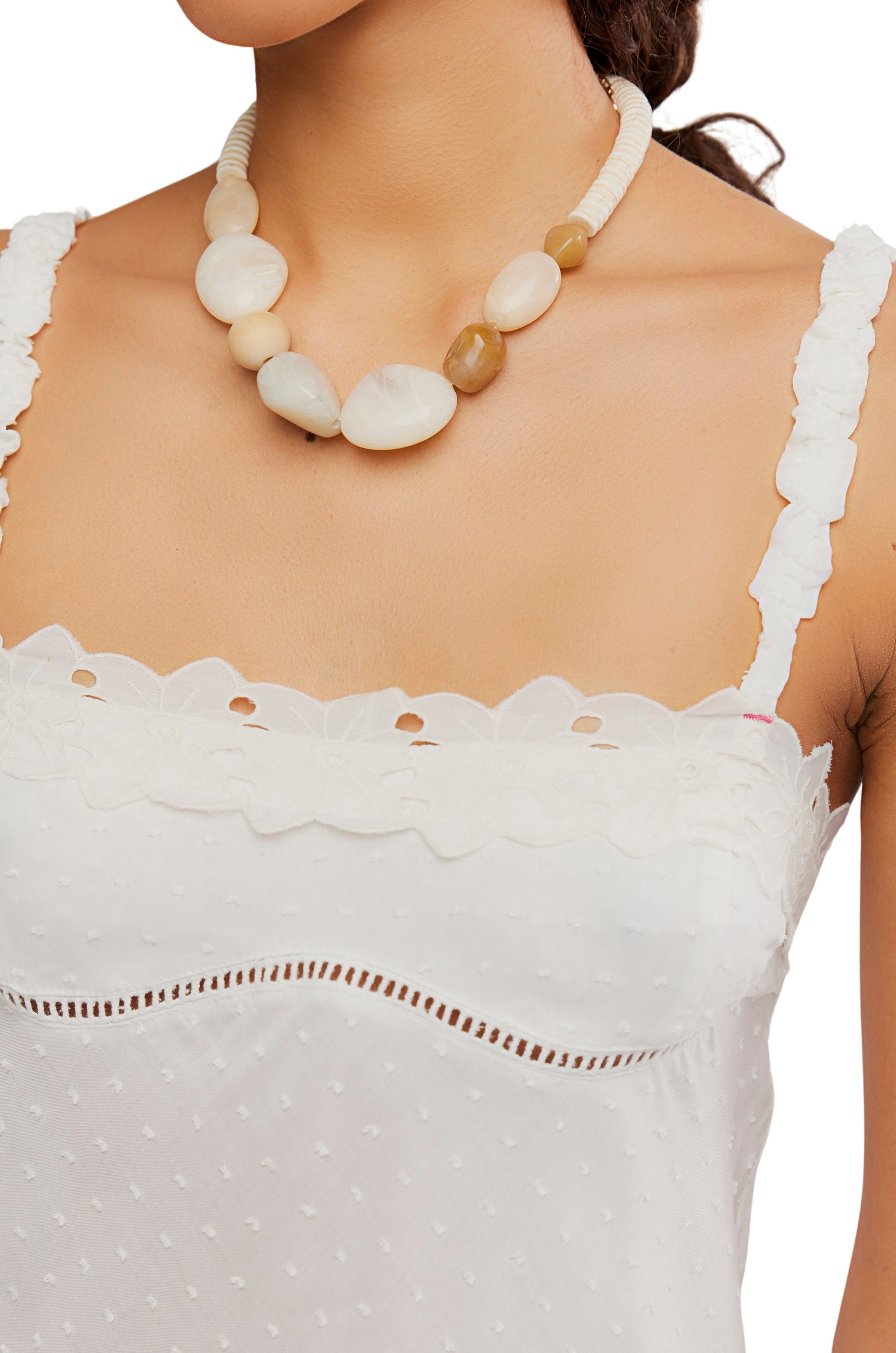 A woman wears the Free People Little Love Tank, a sleeveless white textured pull-on top with lace trim, paired with a chunky beaded necklace in white and beige. Only her neck, shoulders, and upper chest are visible.