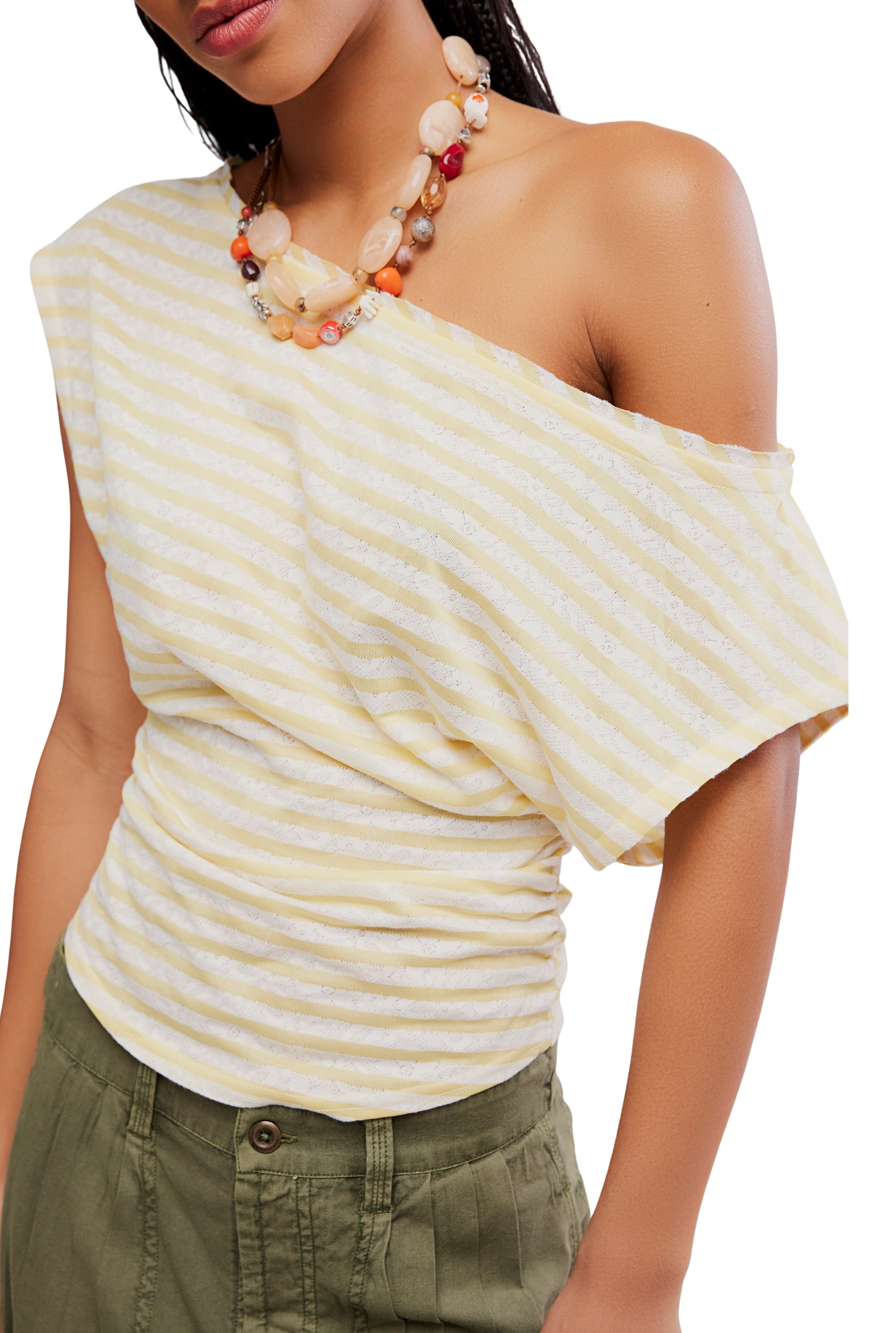 A woman wears the Free People Ellie Top in Yellow Multi—an off-the-shoulder, ruched style—paired with olive pants and a chunky neutral beaded necklace. Her head is partially out of frame.