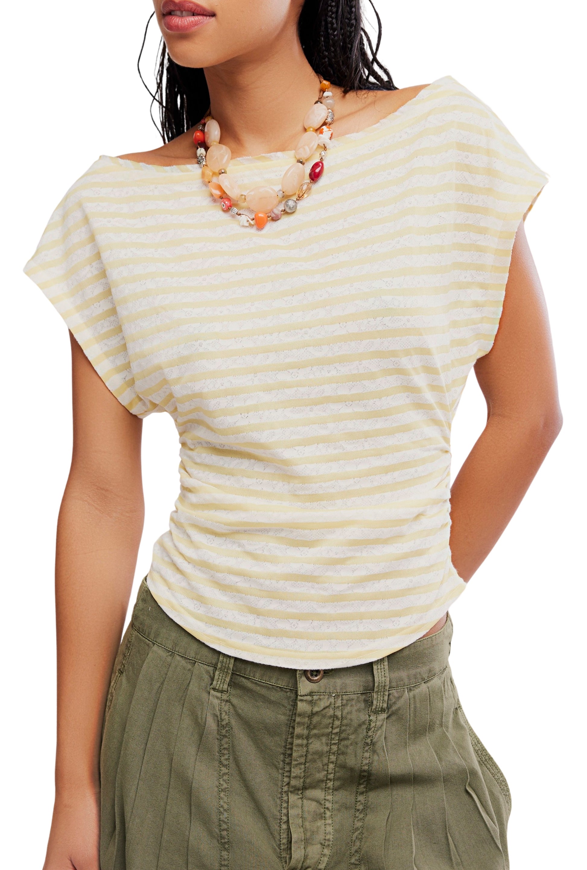 A woman wears the Free People Ellie Top, a yellow and white striped, stretchy knit short-sleeve shirt, paired with olive green pleated pants and a chunky beige and orange beaded necklace. Shown from shoulders to upper thighs.