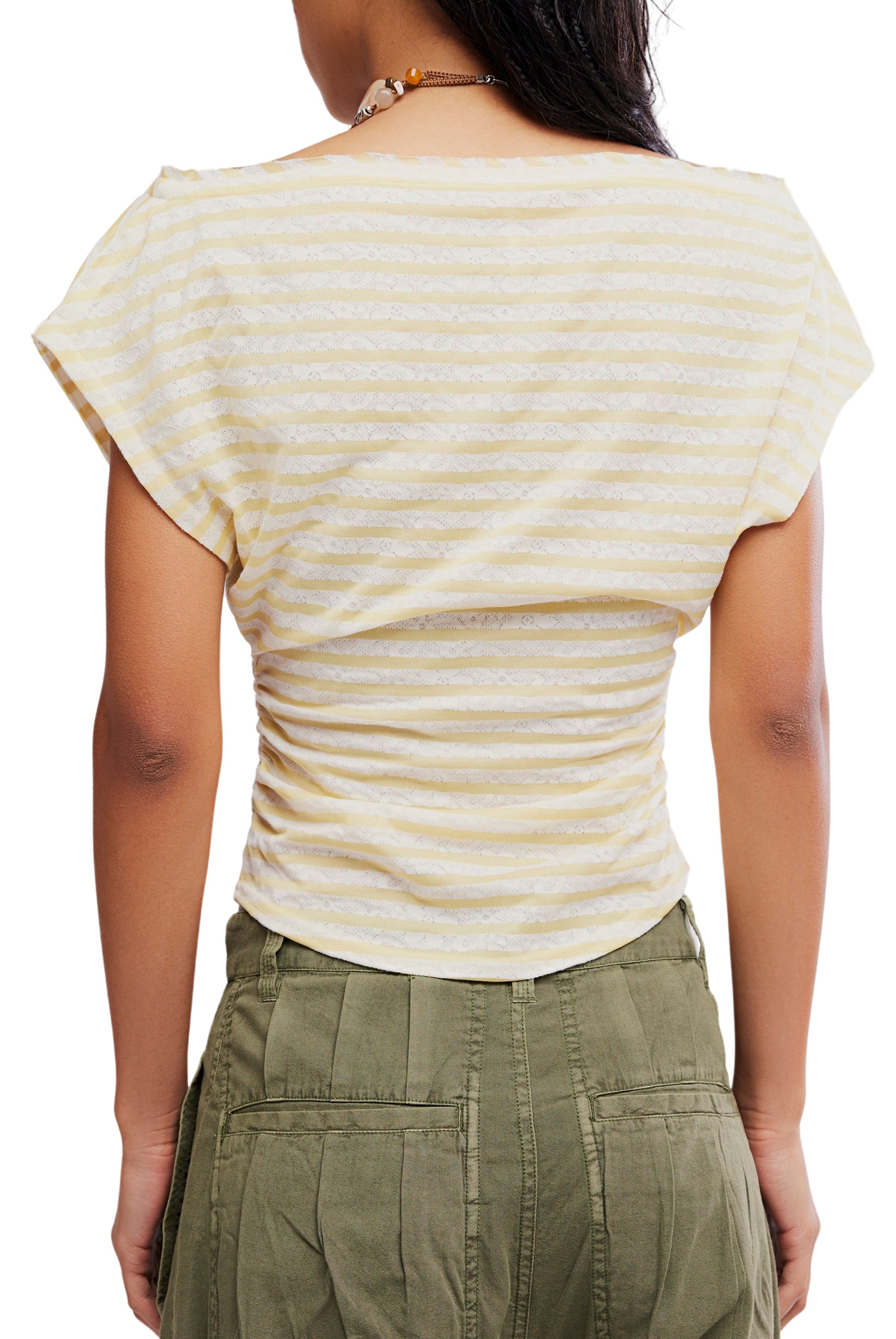 A person wearing the Free People Ellie Top—a light yellow and white striped, short-sleeve, ruched-side knit—paired with high-waisted olive green pants. Shown from the back, it highlights the top’s flattering details.