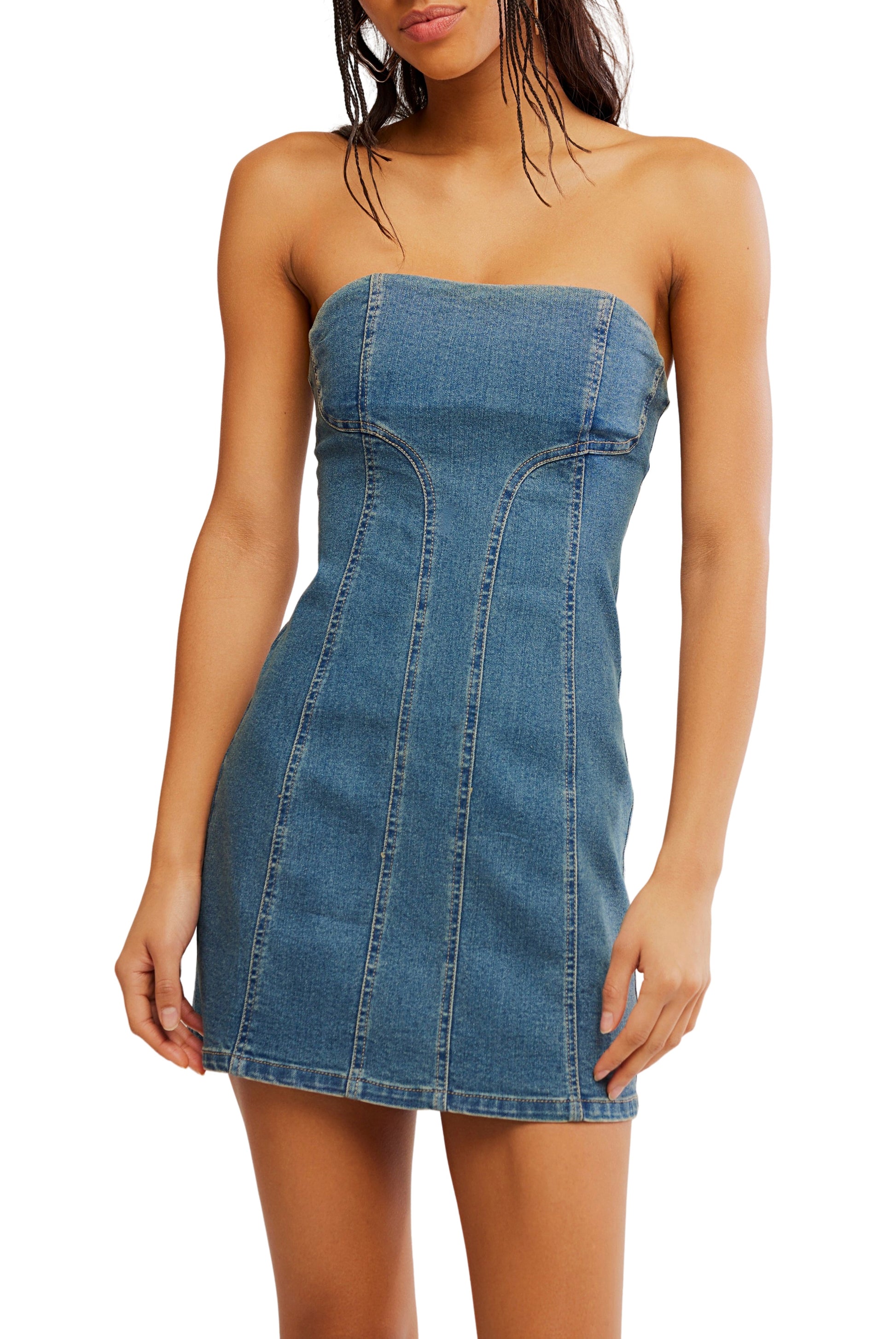 A woman wears the Alexa Mini Dress by Free People in Medium Denim—a classic, strapless mini with a fitted column silhouette and vertical seam detailing. The casual, sleeveless dress ends above the knee. Her hair is loose, arms relaxed by her sides.