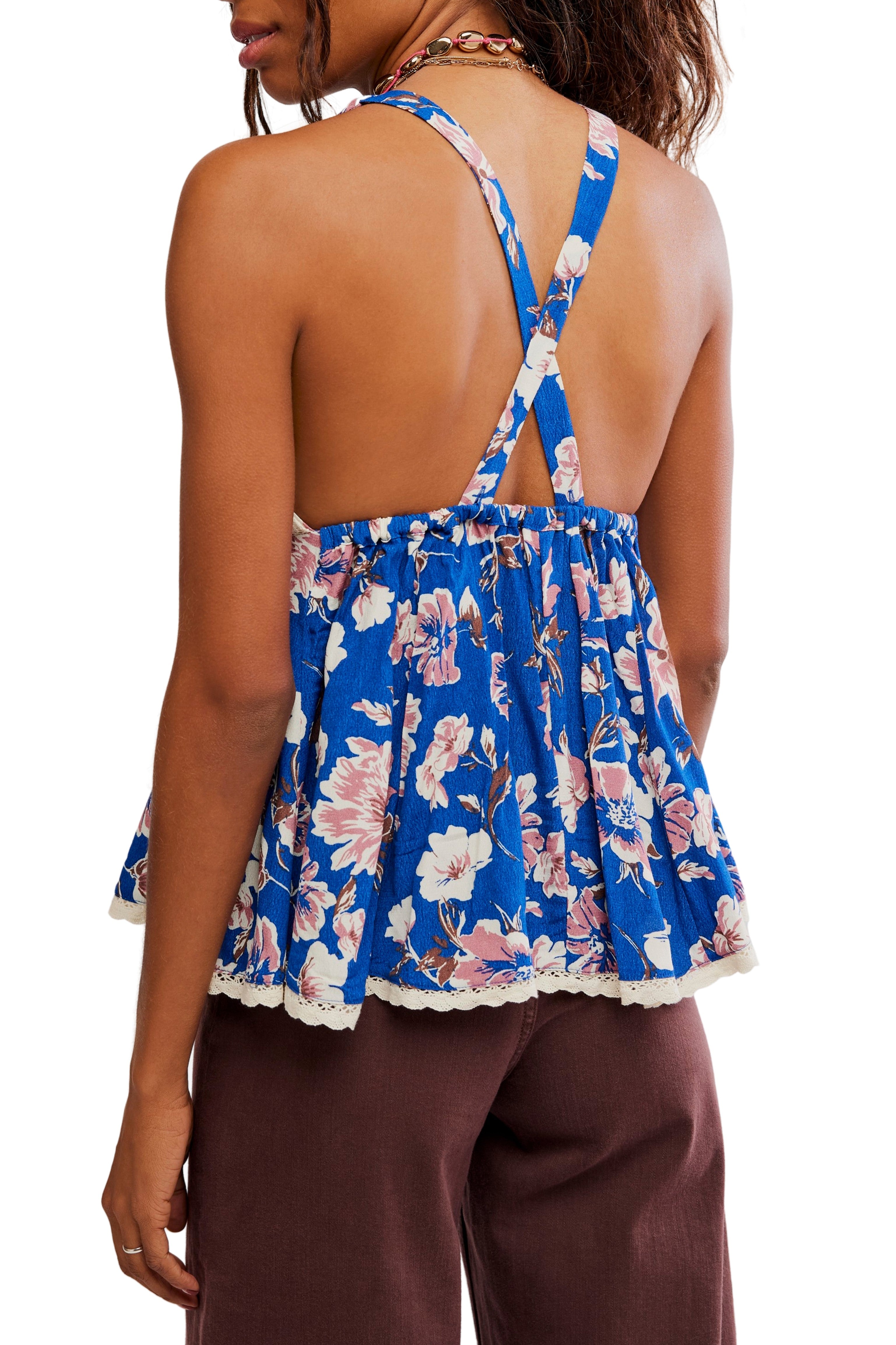 Wearing the Rome Printed Tank by Free People—a blue floral halter top with a plunging neckline, crisscross straps, lace trim, open back, and lightweight 100% viscose fabric—paired with brown pants.