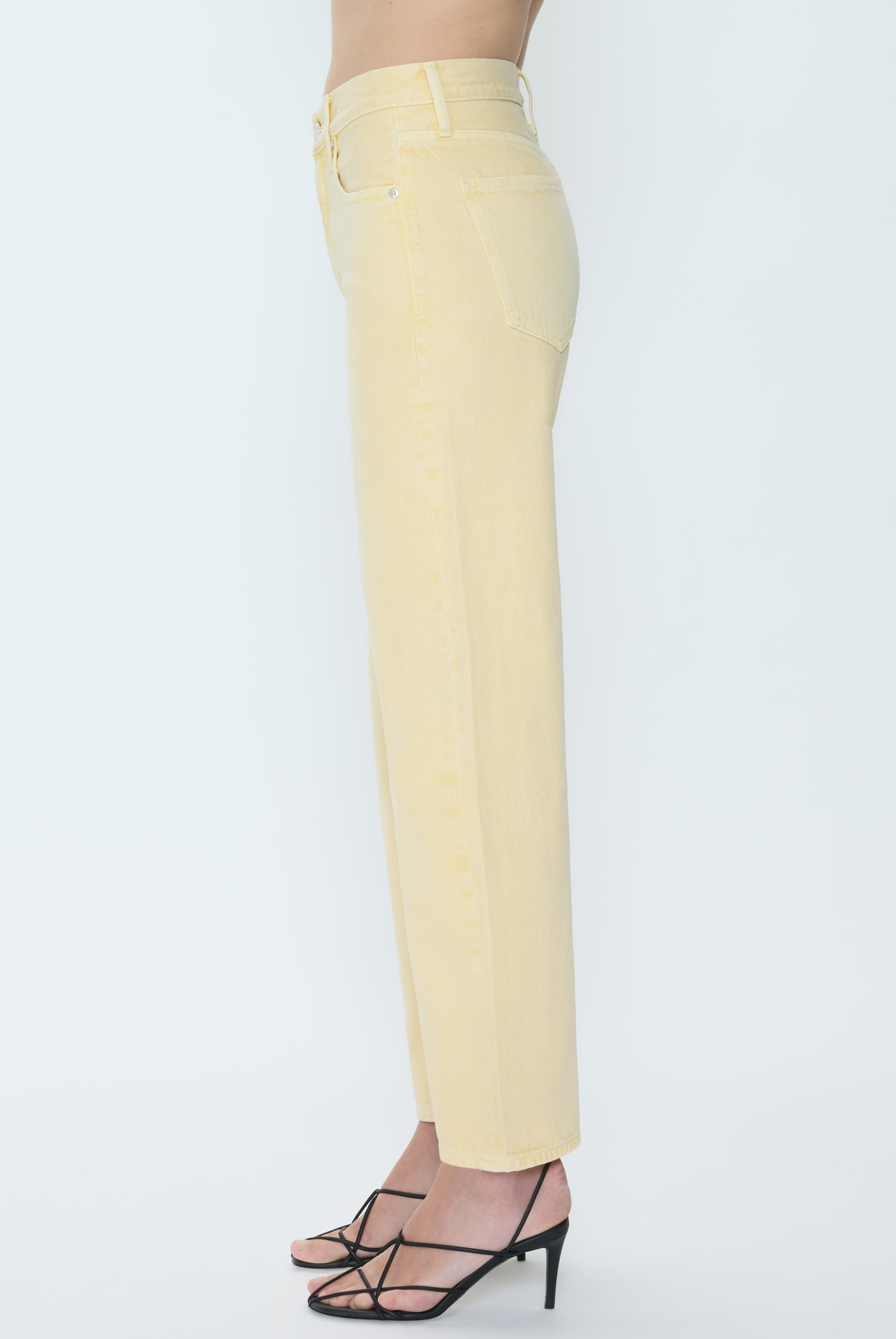 A person wearing Pistola's Lexi - Mid Rise Bowed Straight jeans in pale yellow with black strappy high-heeled sandals, shown from the side against a plain white background.