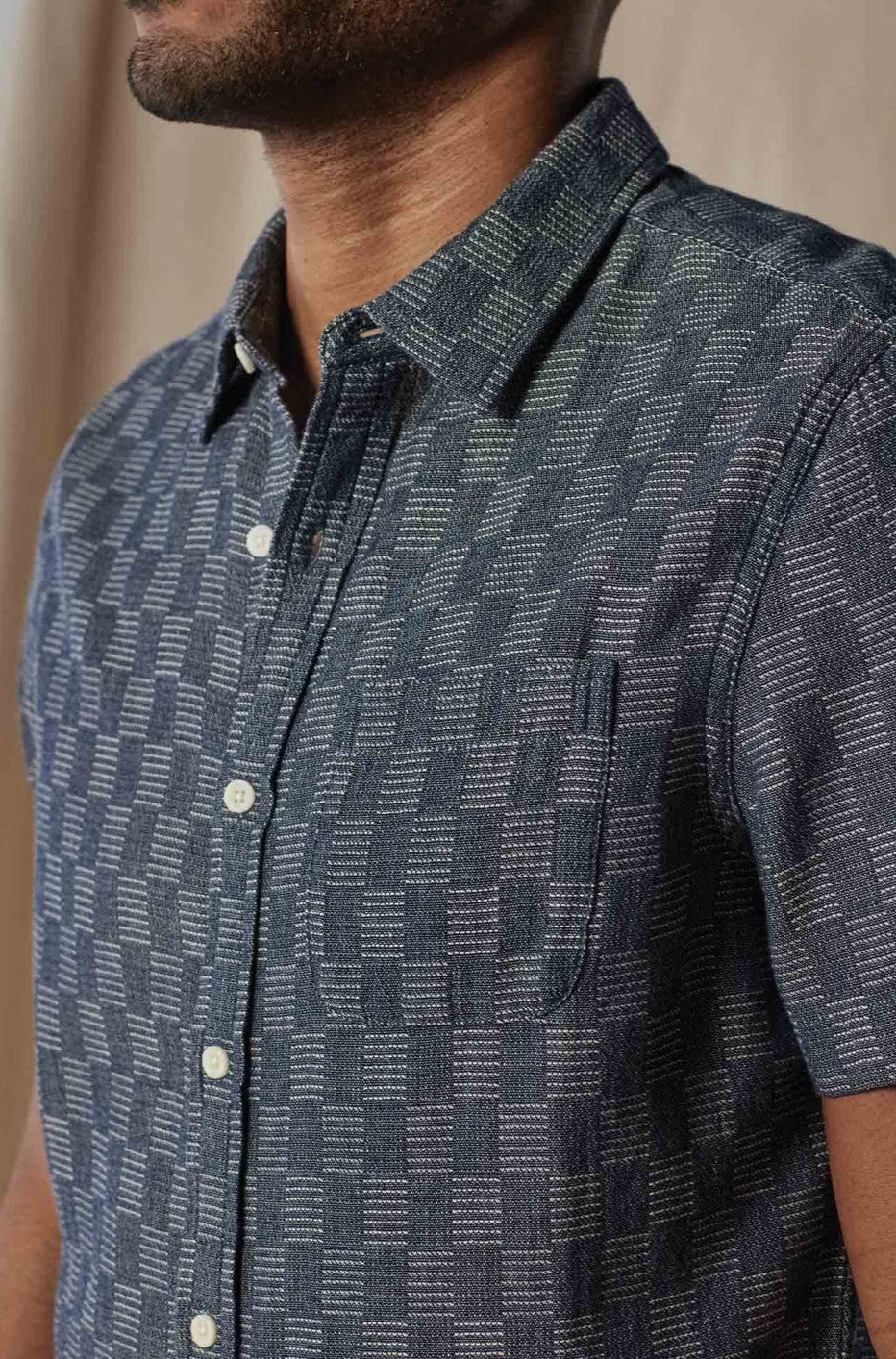 A person wears The Normal Brand’s Freshwater Button Up Ivory Crinkle—a 100% cotton, short-sleeve shirt featuring a front pocket, white buttons, and a classic shirttail hem. Face is partially out of frame.
