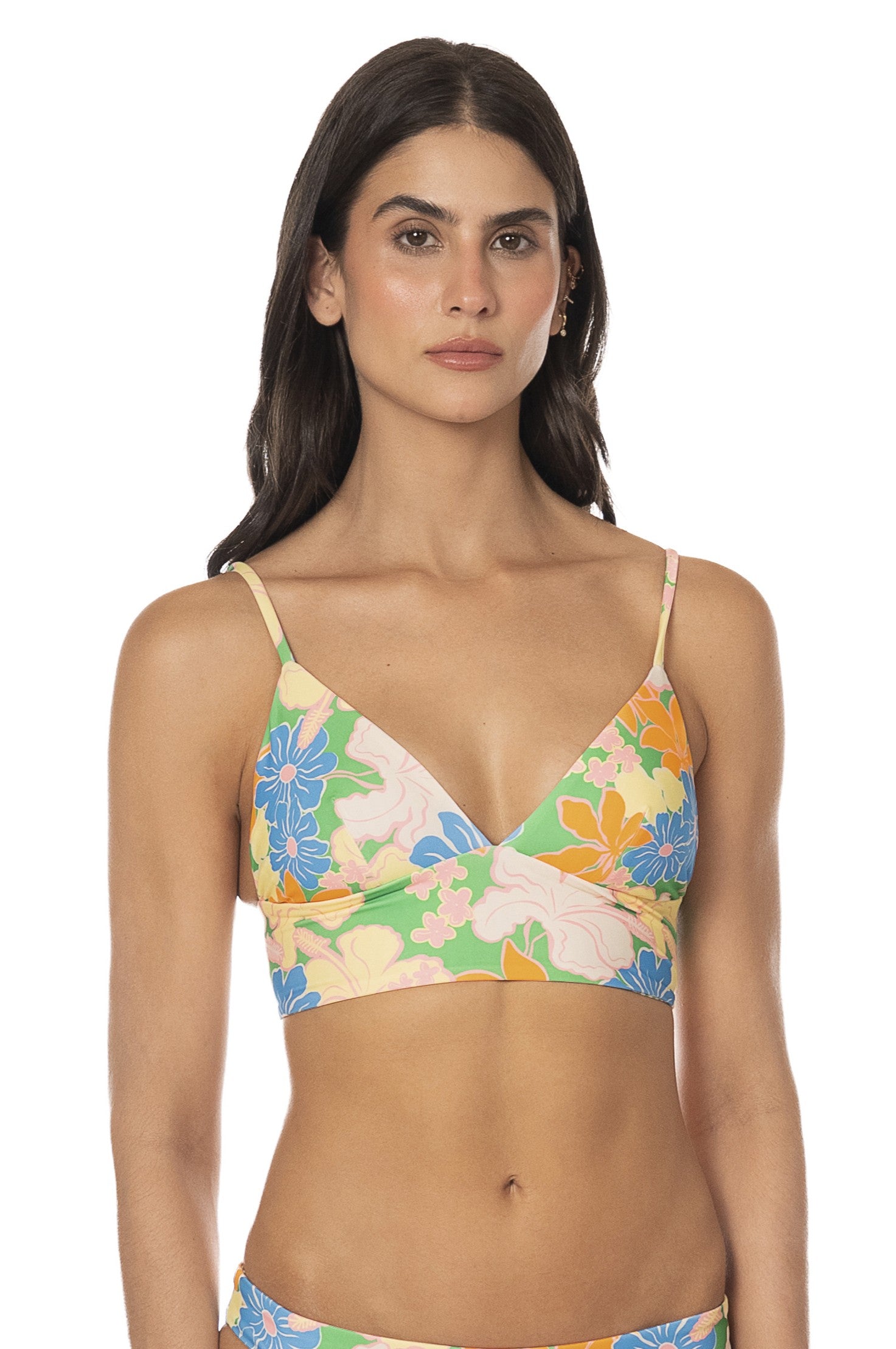 A woman with long dark hair wears the Tropic Lei Mirage Top, a vibrant floral reversible bikini with adjustable straps. She stands against a plain white background, looking directly at the camera with a neutral expression.