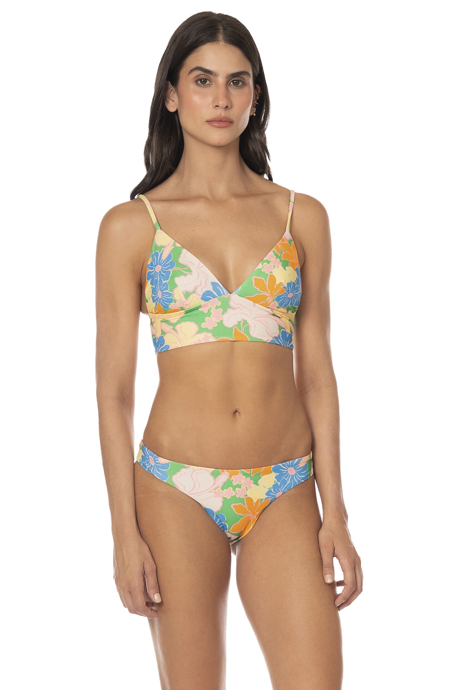A woman faces forward wearing the Tropic Lei Flirt Bottom, a colorful floral reversible bikini bottom with cheeky coverage, paired with a v-neck top. She stands against a plain white background.