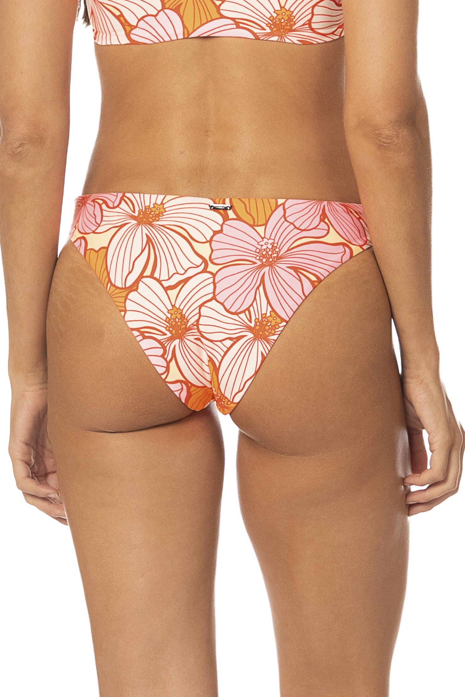 A person is shown from the waist down wearing the Maaji Retro Bloom Sublimity Bottom, a reversible bikini bottom with a pink and orange floral pattern and cheeky coverage, against a plain white background.