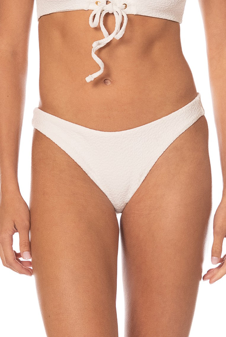 A person models the Maaji Coconut Milk Sublimity Bottom bikini in white, featuring a reversible pebble texture, shown from mid-torso to upper thighs against a plain white background.