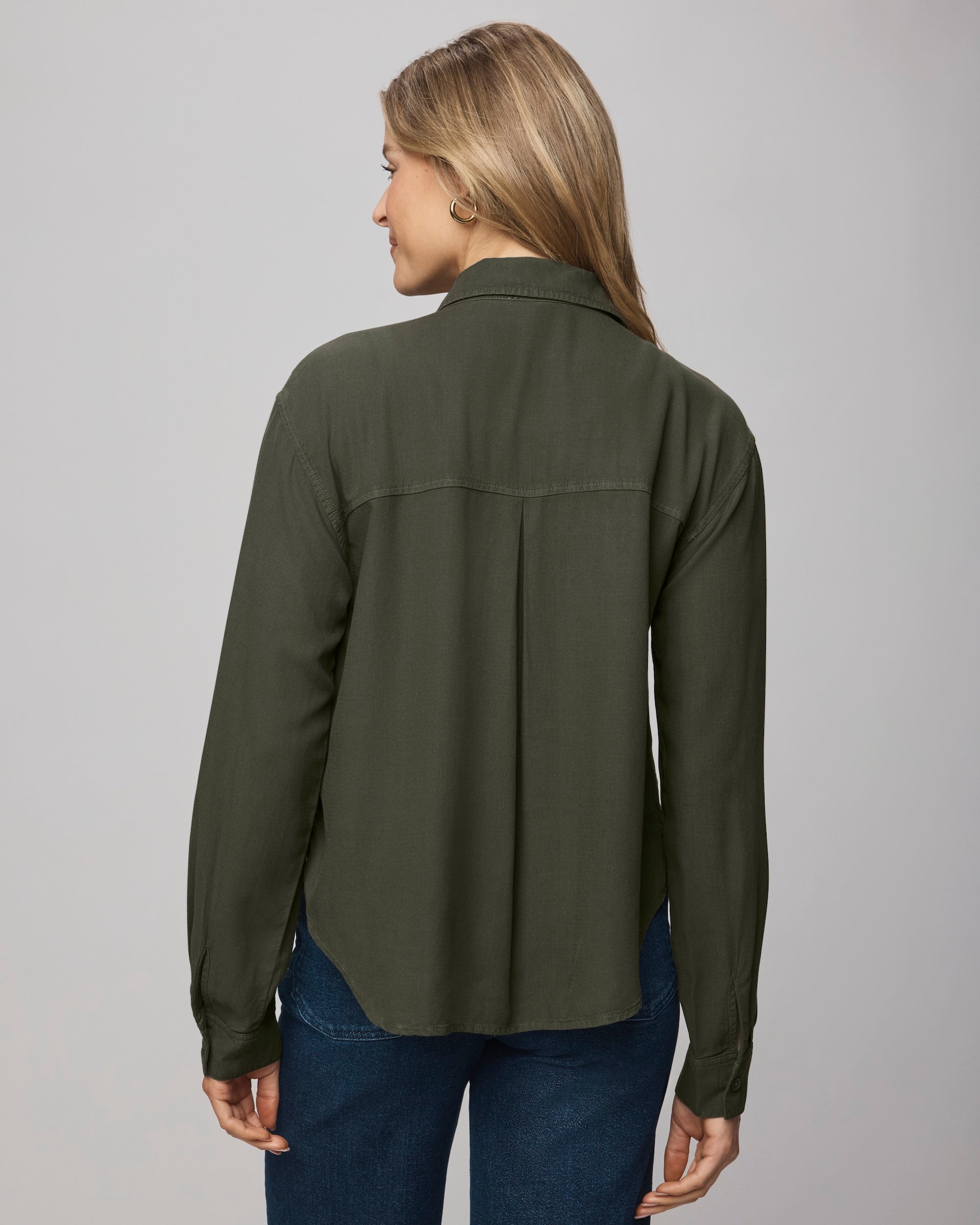 A person with long, light brown hair wears the Splendid Joanne Blouse in dark green and blue jeans, standing against a plain light background and looking over their left shoulder.