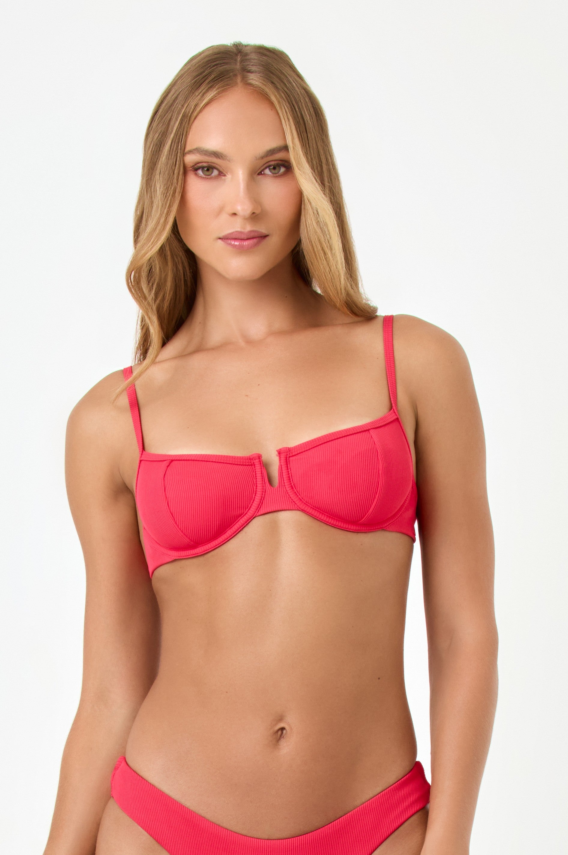 A woman with long, wavy blonde hair wears the LSpace Pout Hunter Top in red with matching bottoms, standing against a plain white background and looking at the camera with a neutral expression.