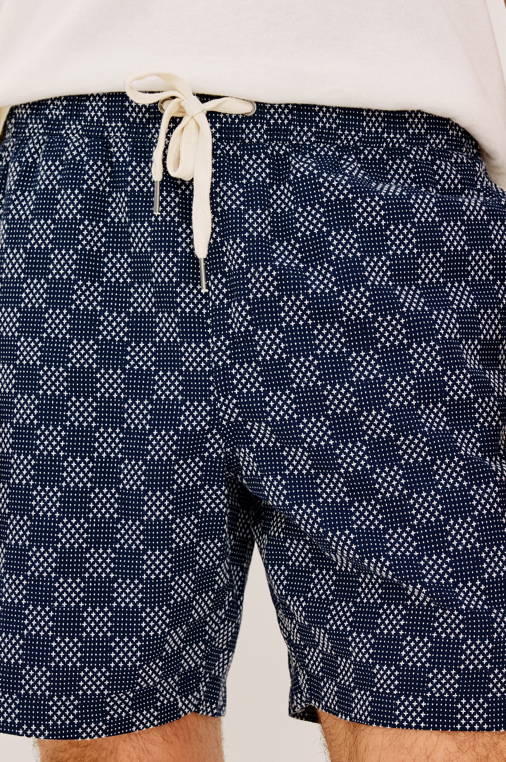 A close-up of a person wearing the Cruz relaxed fit shorts by Rails in navy blue with a white geometric dot pattern and drawstring, paired with a white shirt.