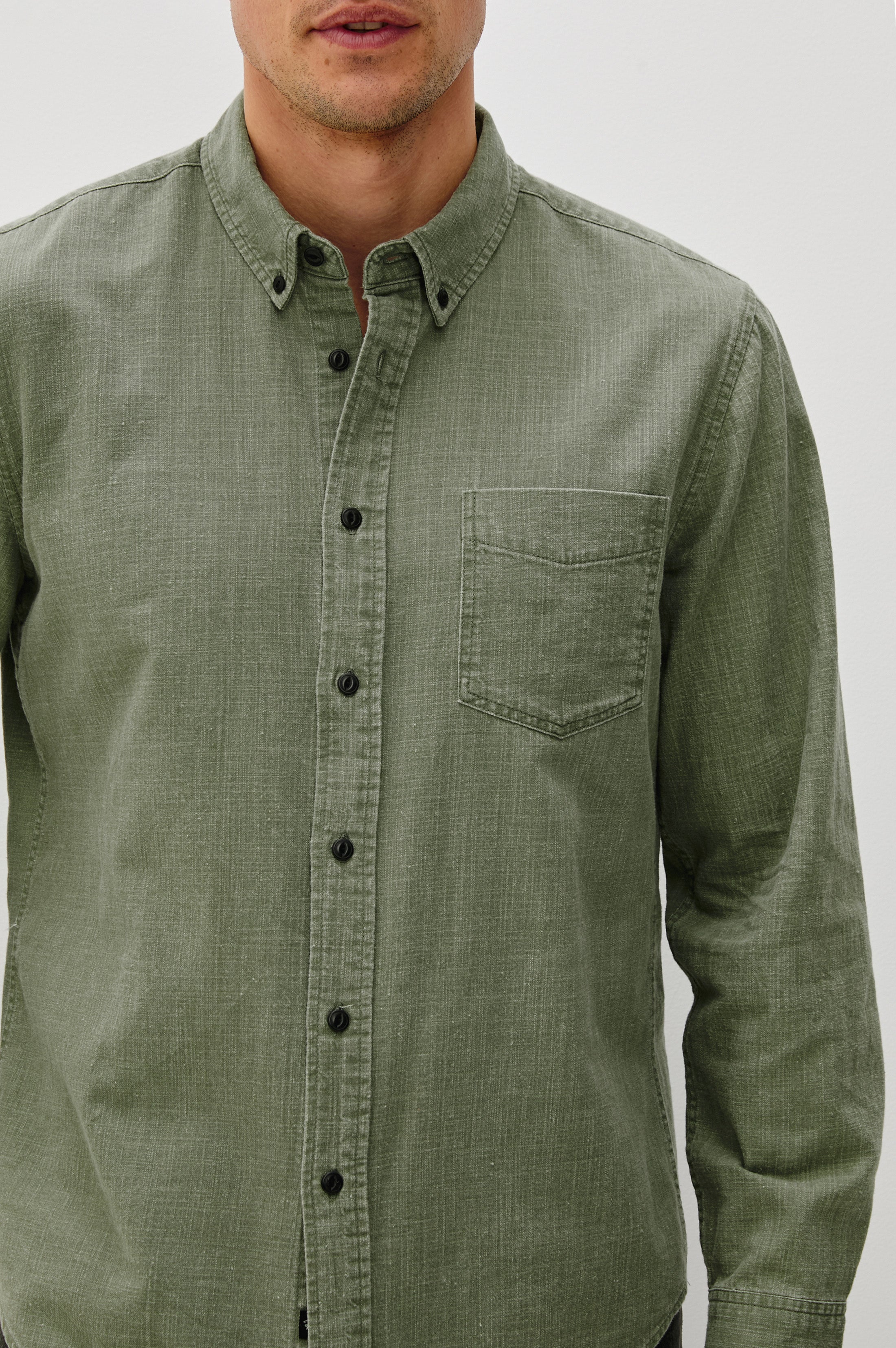 A person models the Rails Tristan Button Down Shirt in relaxed fit, long-sleeve olive green 100% cotton with a chest pocket, standing against a white background. Face is partially out of frame. Machine wash cold for easy care.