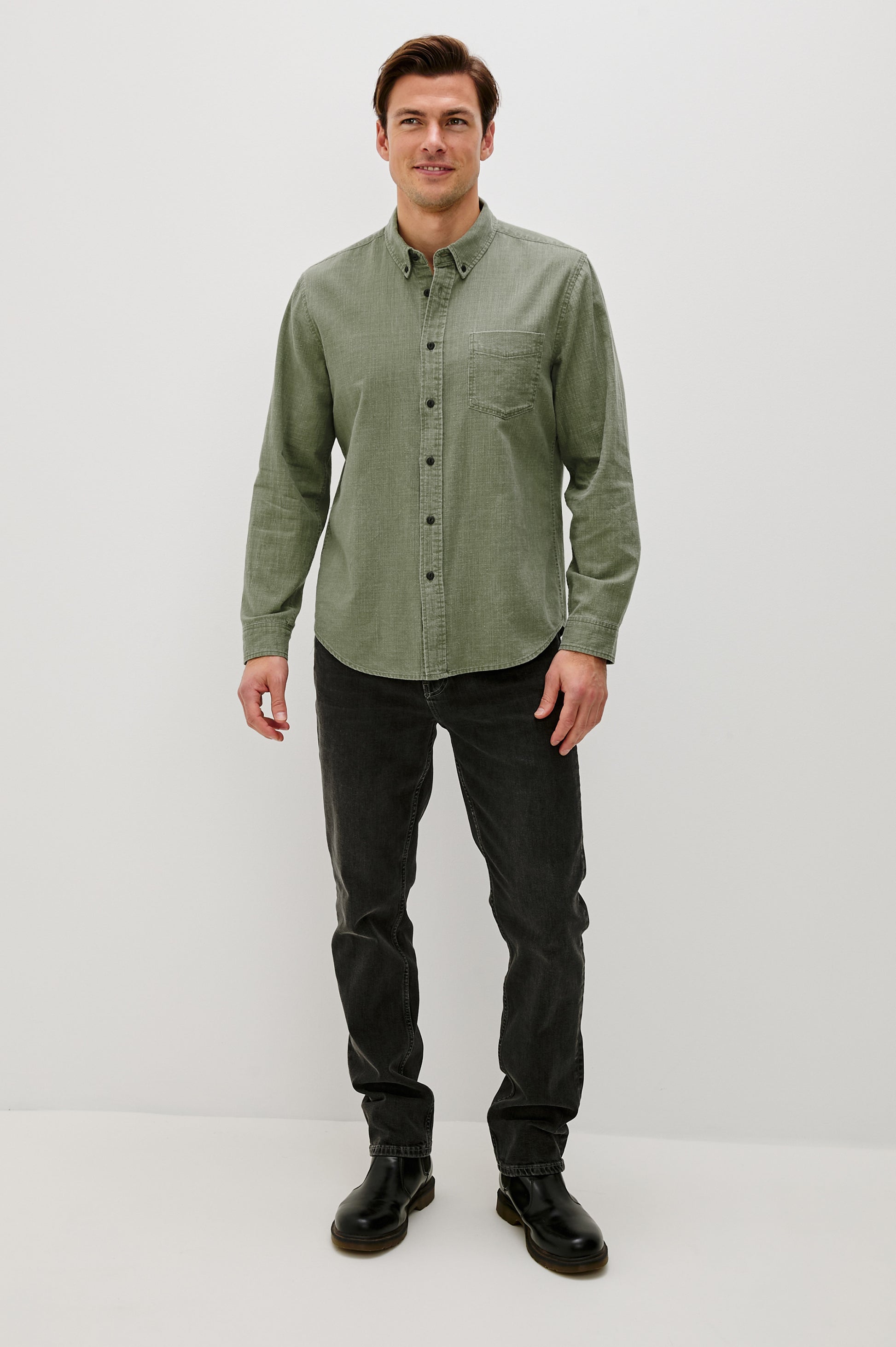 A man faces forward wearing the Rails Tristan Button Down Shirt in light green, a relaxed fit 100% cotton style, paired with dark jeans and black boots against a plain white background.