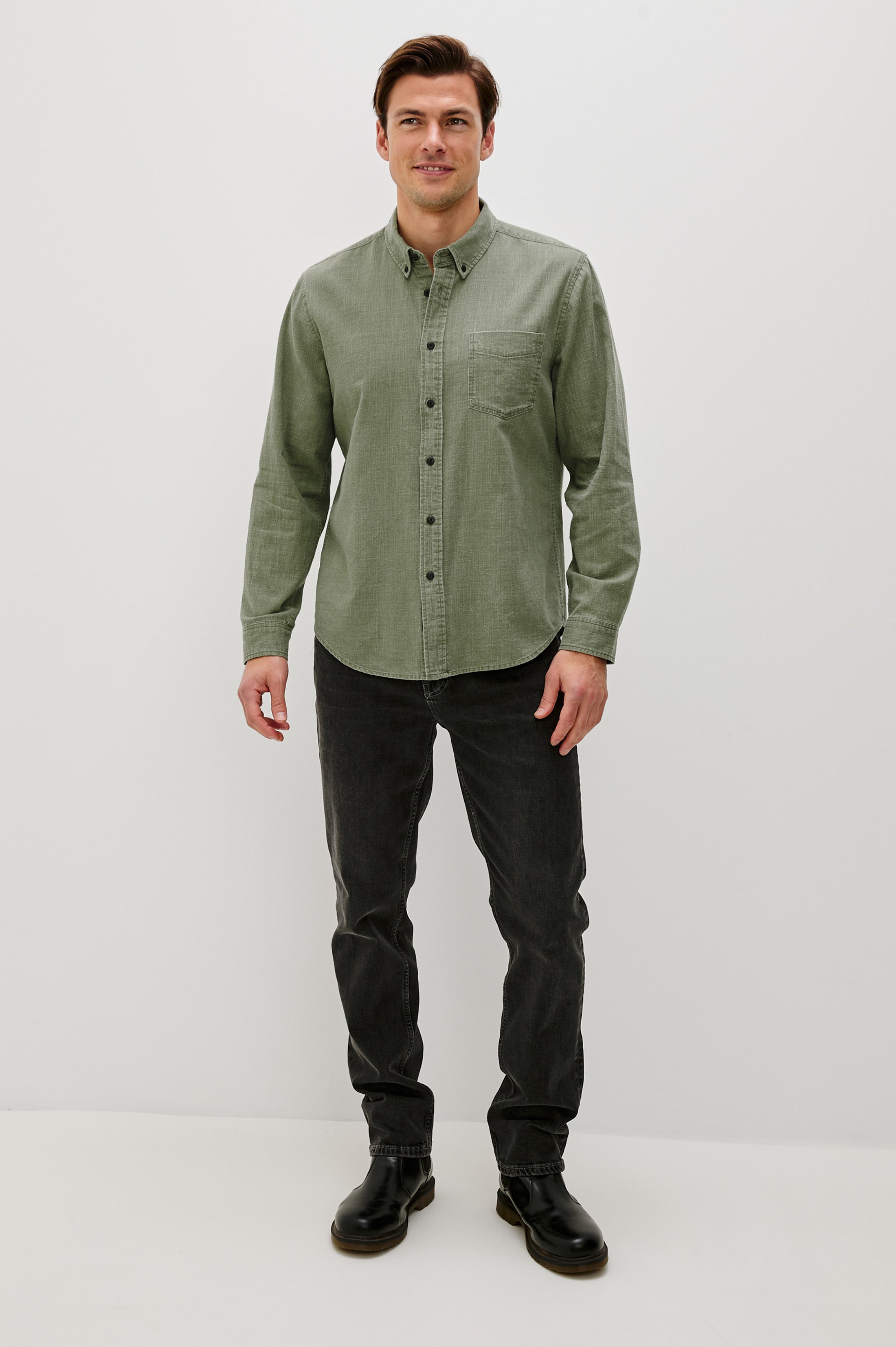 A man faces forward wearing the Rails Tristan Button Down Shirt in light green, a relaxed fit 100% cotton style, paired with dark jeans and black boots against a plain white background.
