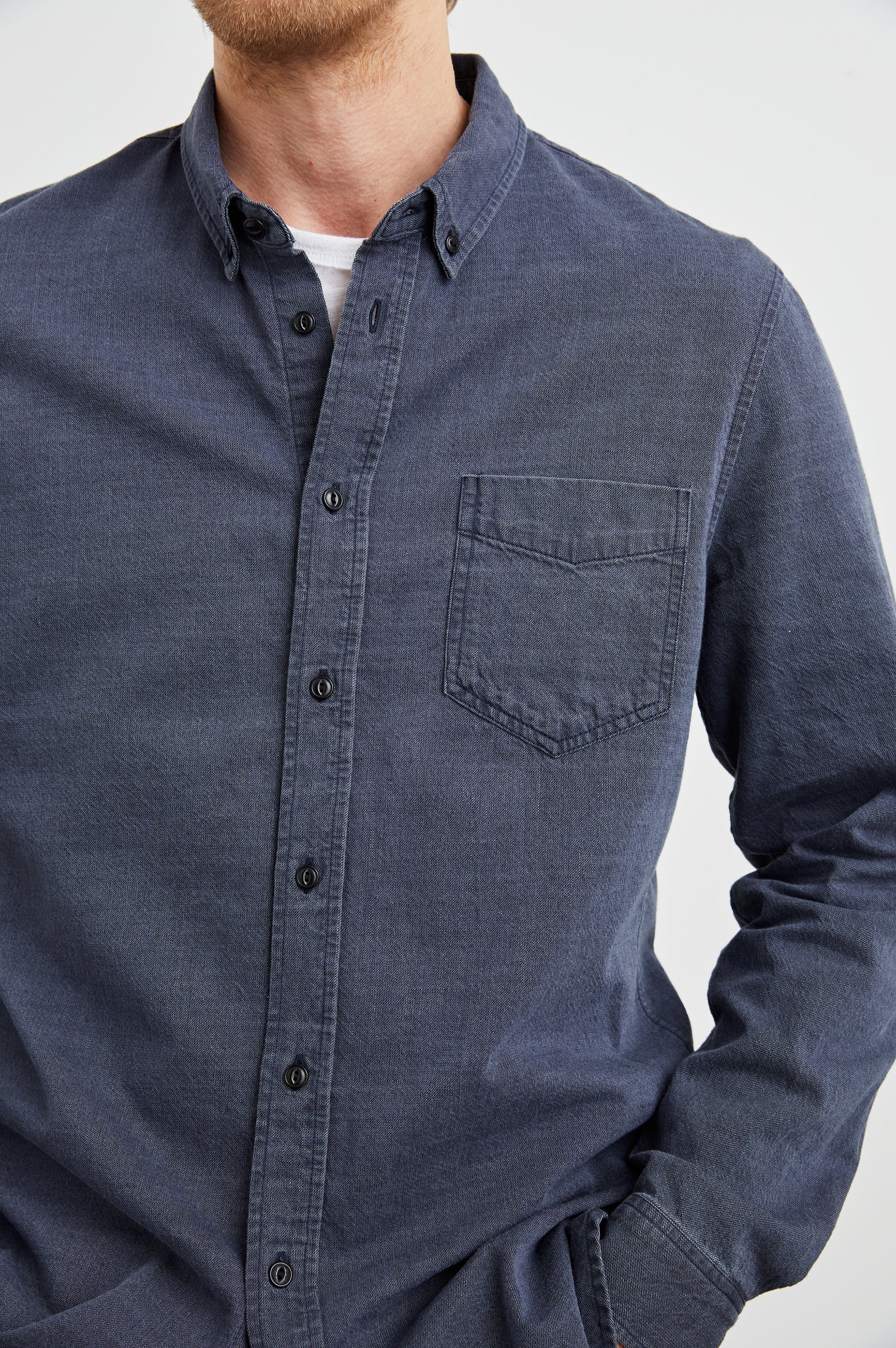 A person wears the Rails Tristan Button Down Shirt—a relaxed fit, dark blue shirt with a front pocket—over a white undershirt, shown from shoulders to waist against a light background. 100% cotton, machine wash cold.