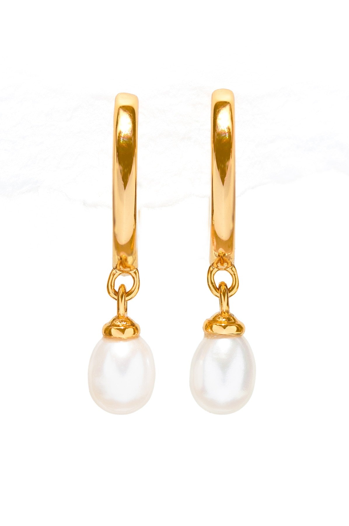 The South Moon Under Pearl Mini Hoops are gold-tone huggie earrings with a single white pearl drop, shown on a white background. Lightweight and stylish, they add effortless elegance to any occasion.