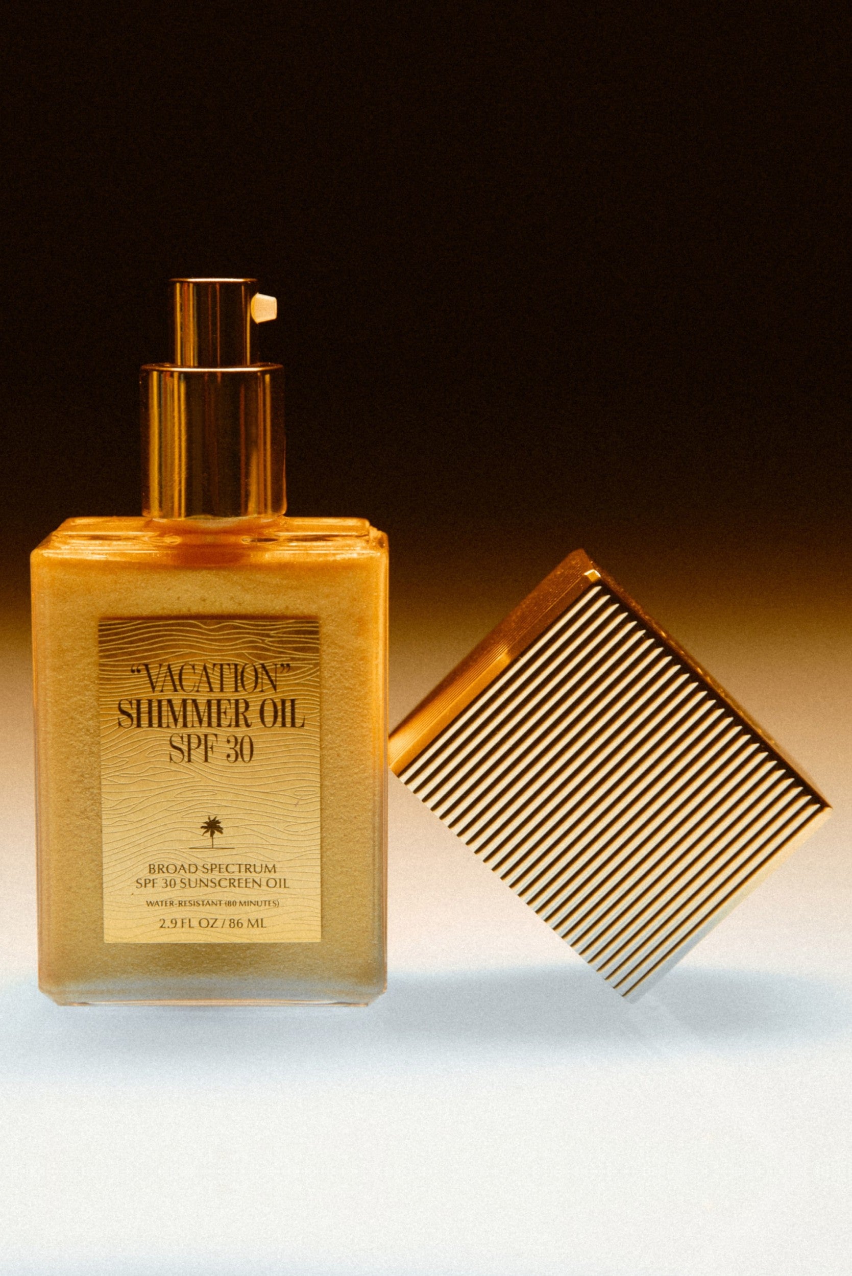 A bottle of Vacation Shimmer Oil SPF 30 by Vacation in multi stands upright beside a shiny gold comb, both set against a gradient brown and white background.