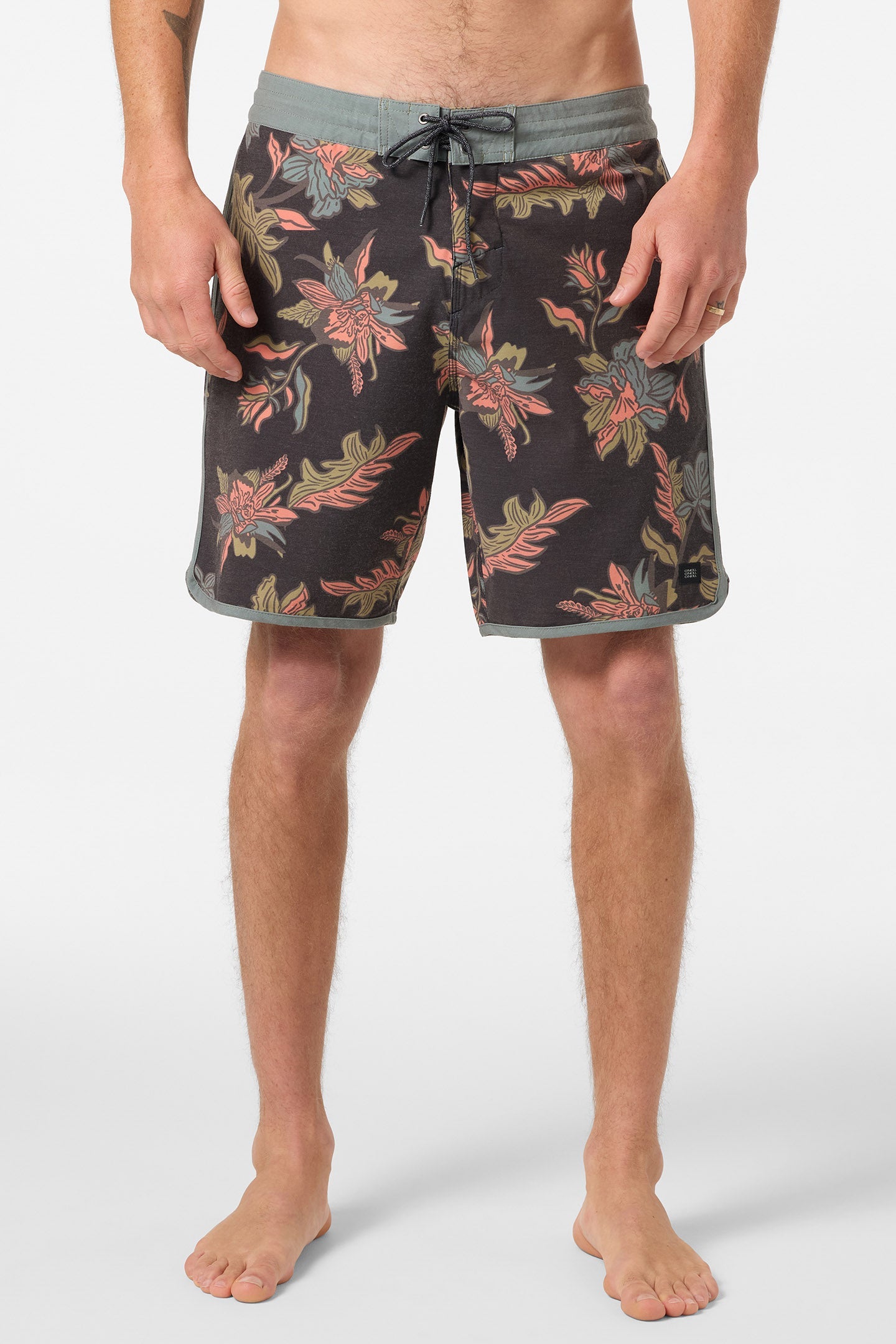 A person stands barefoot in O'Neill Cruzer Scallop 18 In Boardshorts, color Black Multi. The retro shorts have a drawstring waist and a dark floral pattern with red, green, and tan flowers and leaves. Only the lower body is shown.