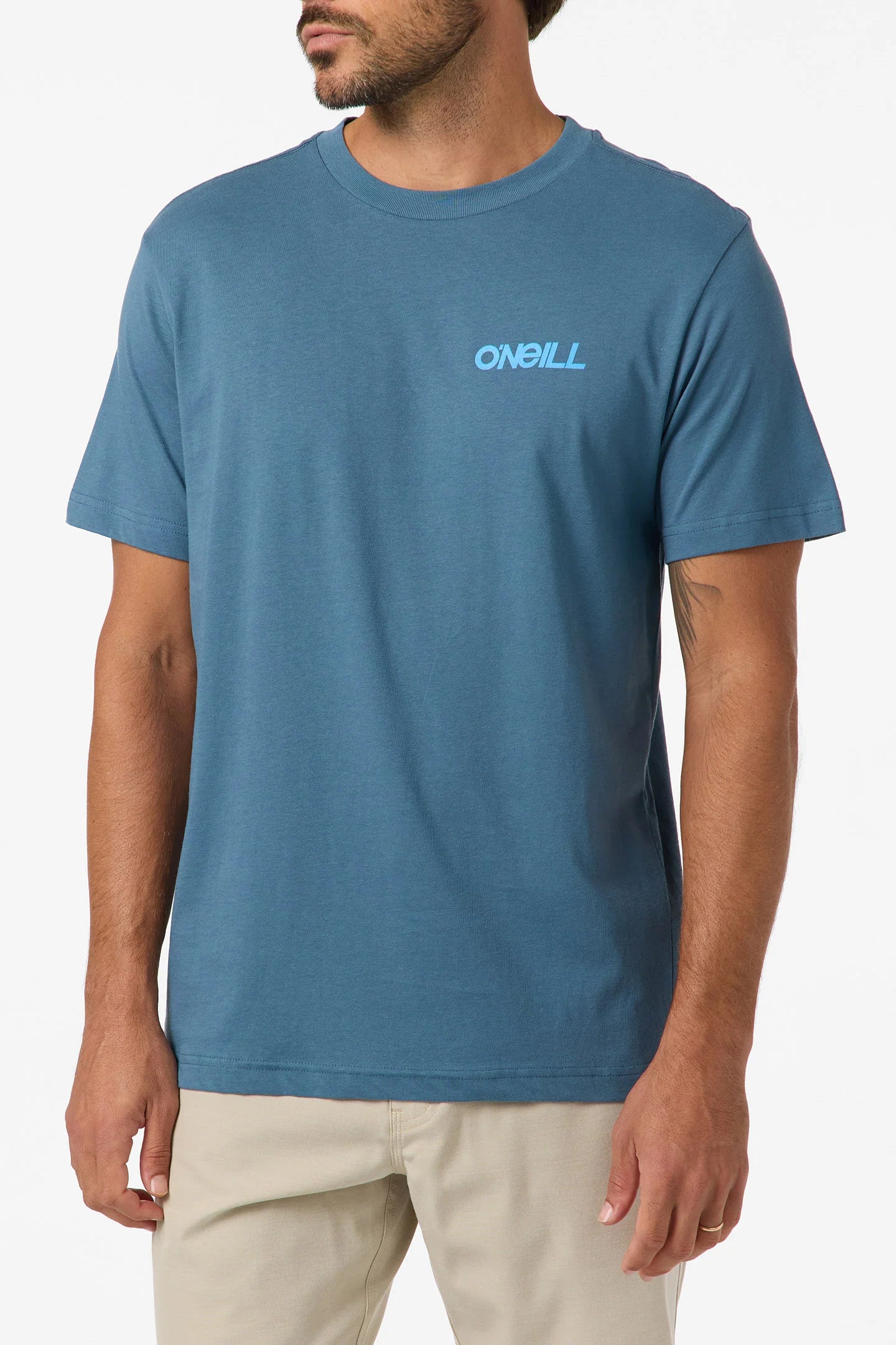 A man wearing the O'Neill Dawn Classic Short Sleeve Tee in blue and beige pants stands against a white background. The standard-fit, 100% cotton shirt features a soft hand screen print O'Neill logo on the left chest.
