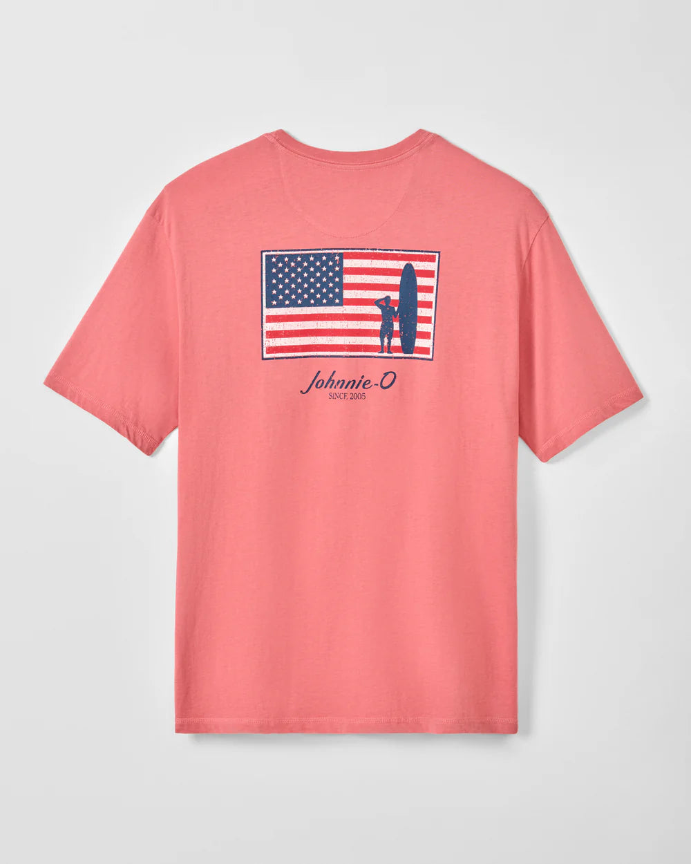 The Johnnie-O American Dream coral pink short sleeve tee features a back surfer dude logo with an American flag, a person holding a surfboard, and “Johnnie-O Since 2005” beneath. Style: JMST100450.
